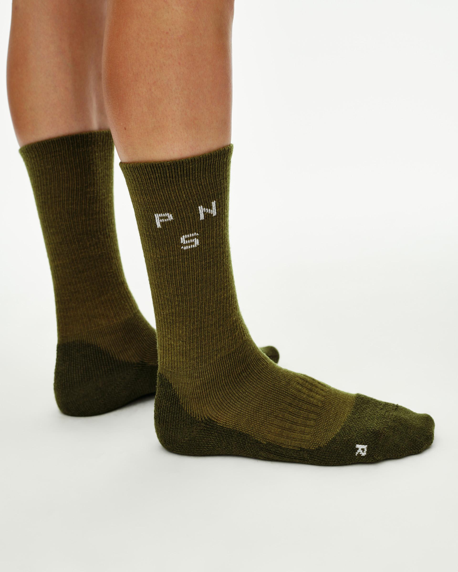 Khaki Green Deep Winter Wool cycling socks on model, side view with white logo knit on cuff