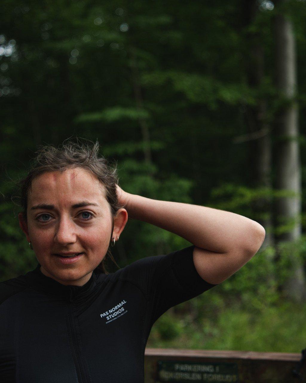 Model wearing black cycling jersey with logo branding in green outdoor setting