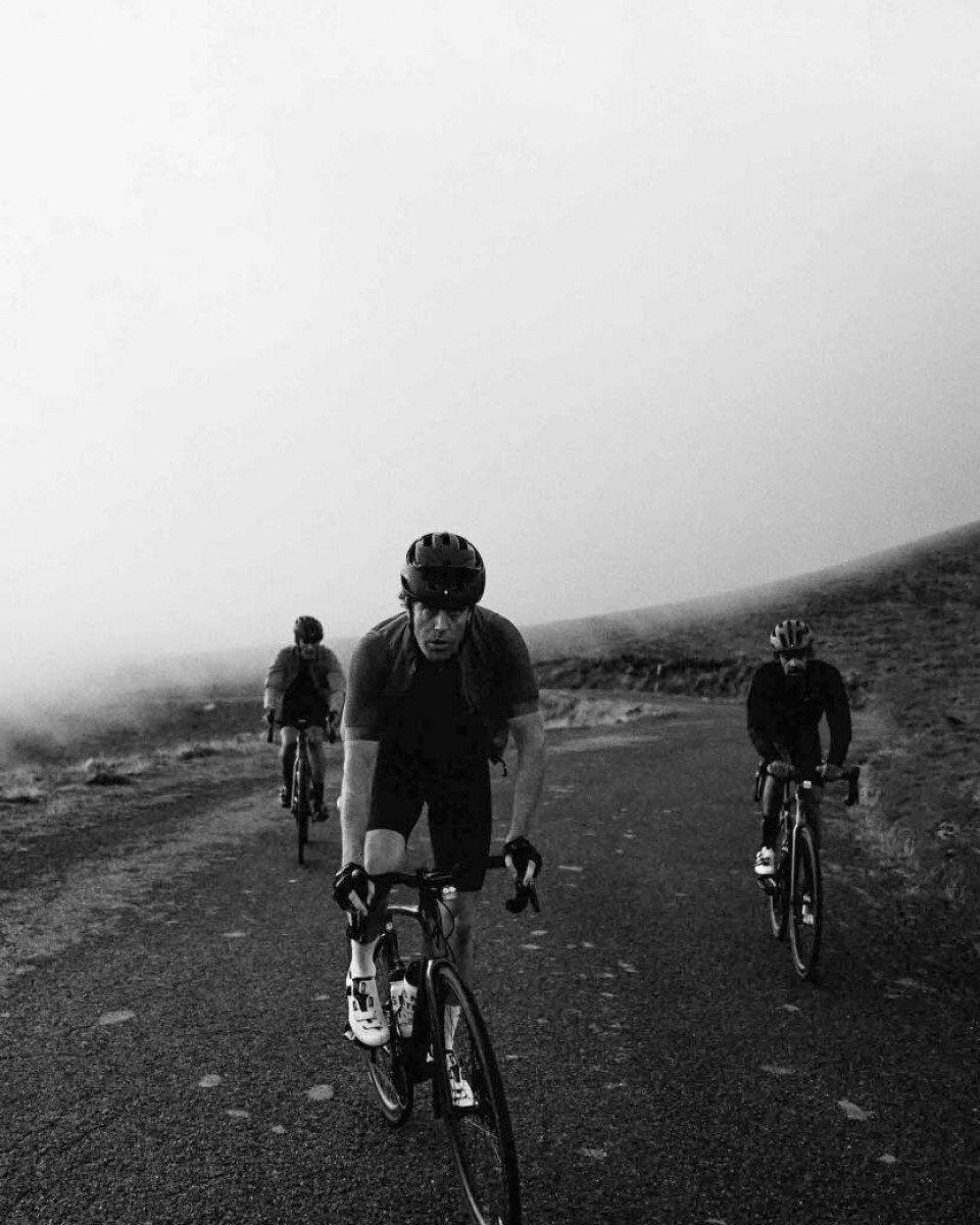Three cyclists in aerodynamic position riding on mountain road in black and white
