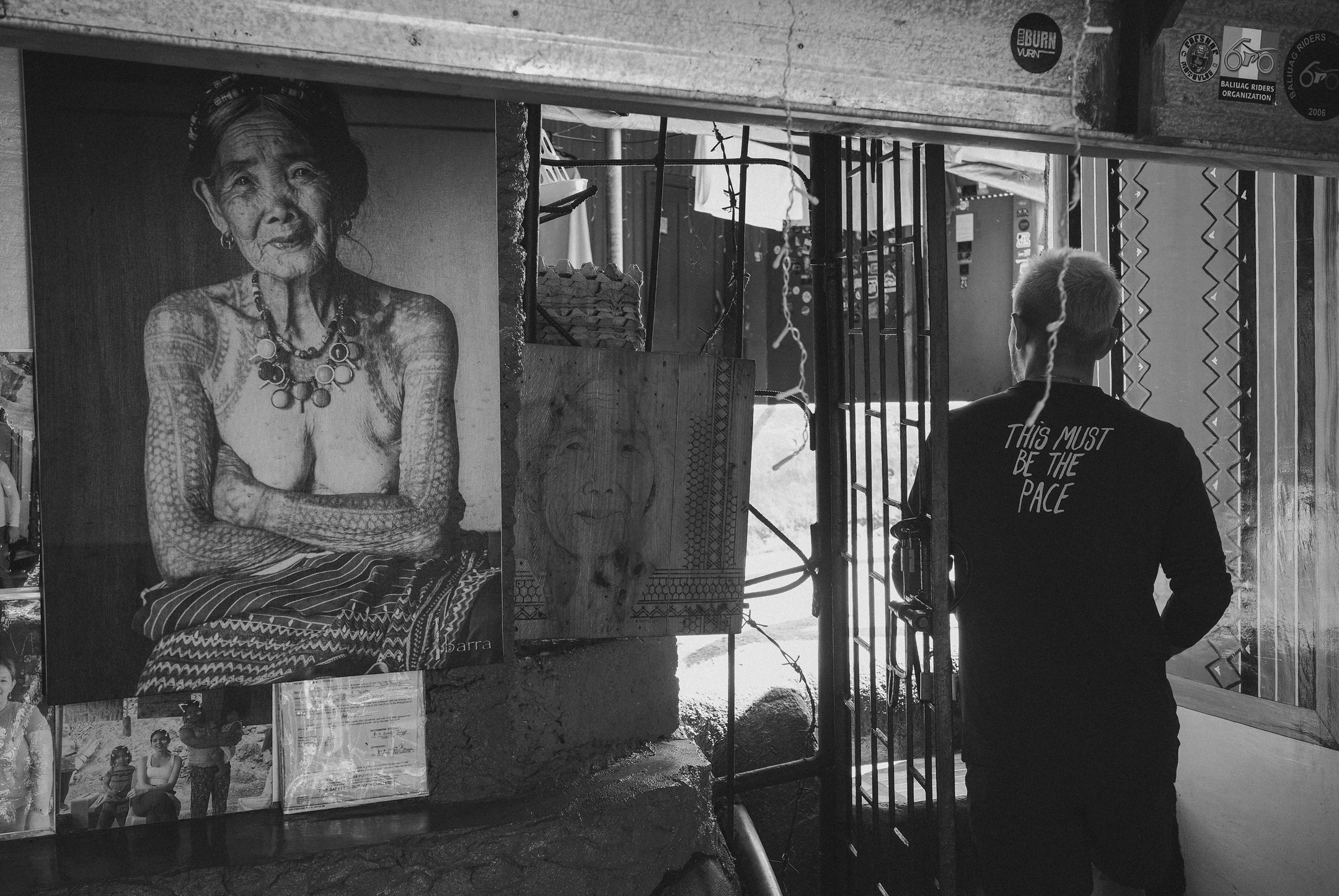 Model wearing black long-sleeve shirt with back text, standing in front of street art display