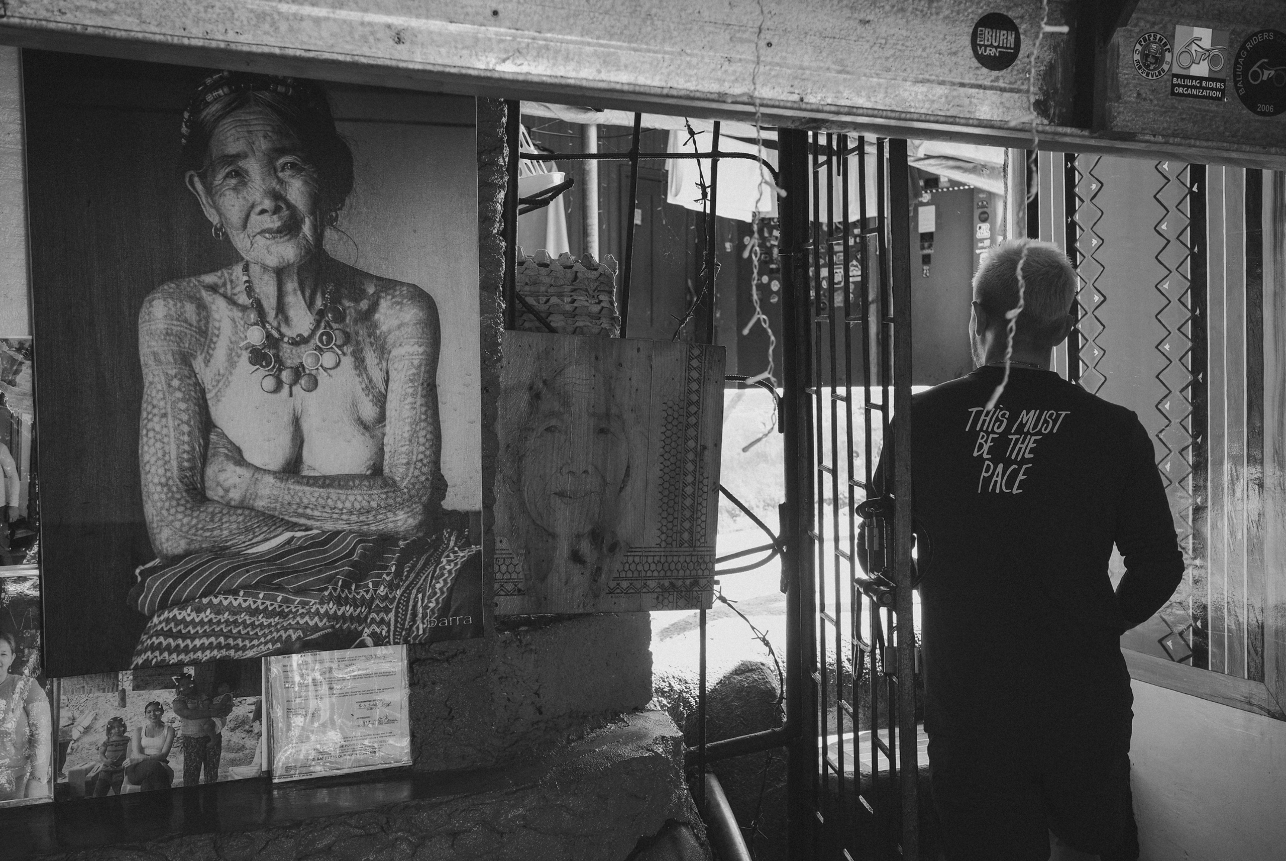 Model wearing black long-sleeve shirt with back text, standing in front of street art display