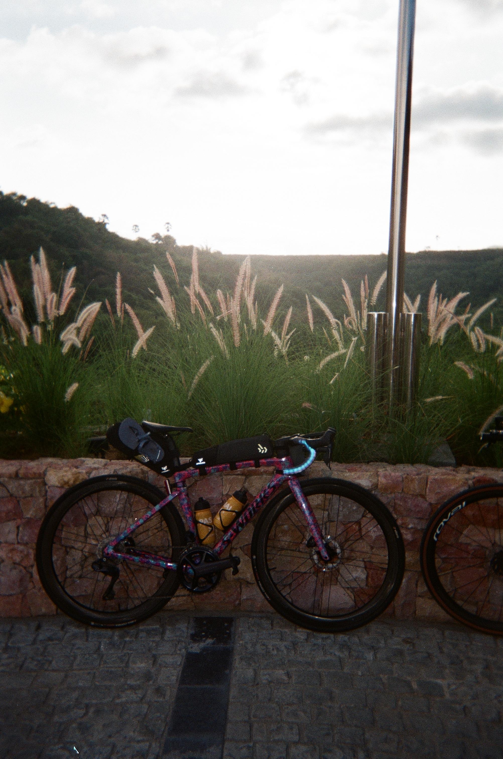 Time trial bike with aerodynamic setup leaning against stone wall in rural Indonesian landscape at dusk