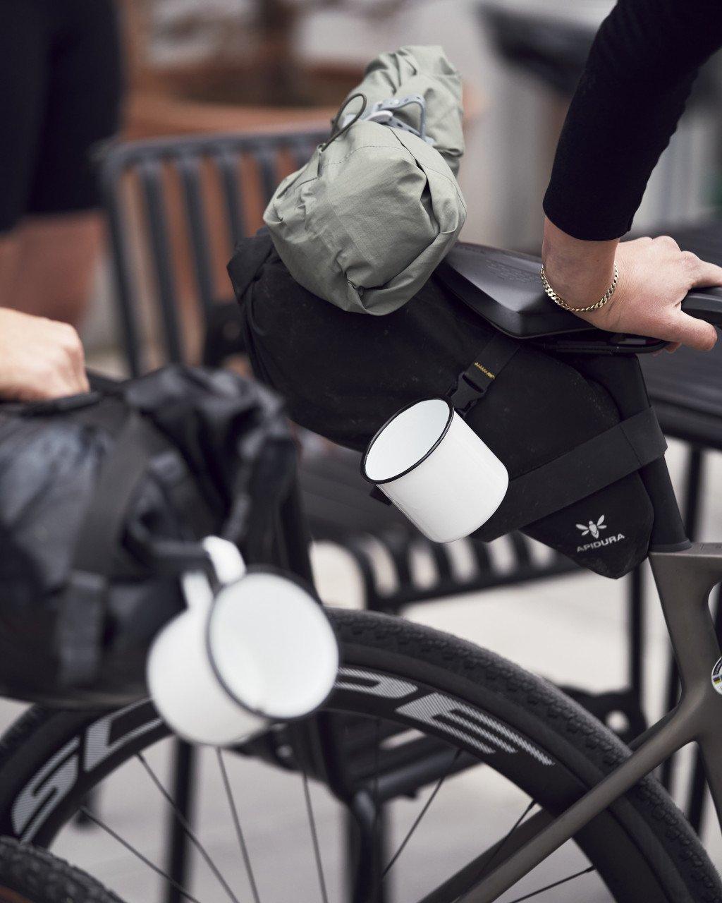 Black handlebar bag with olive green compression sack attached, mounted on bicycle handlebars with white water bottle