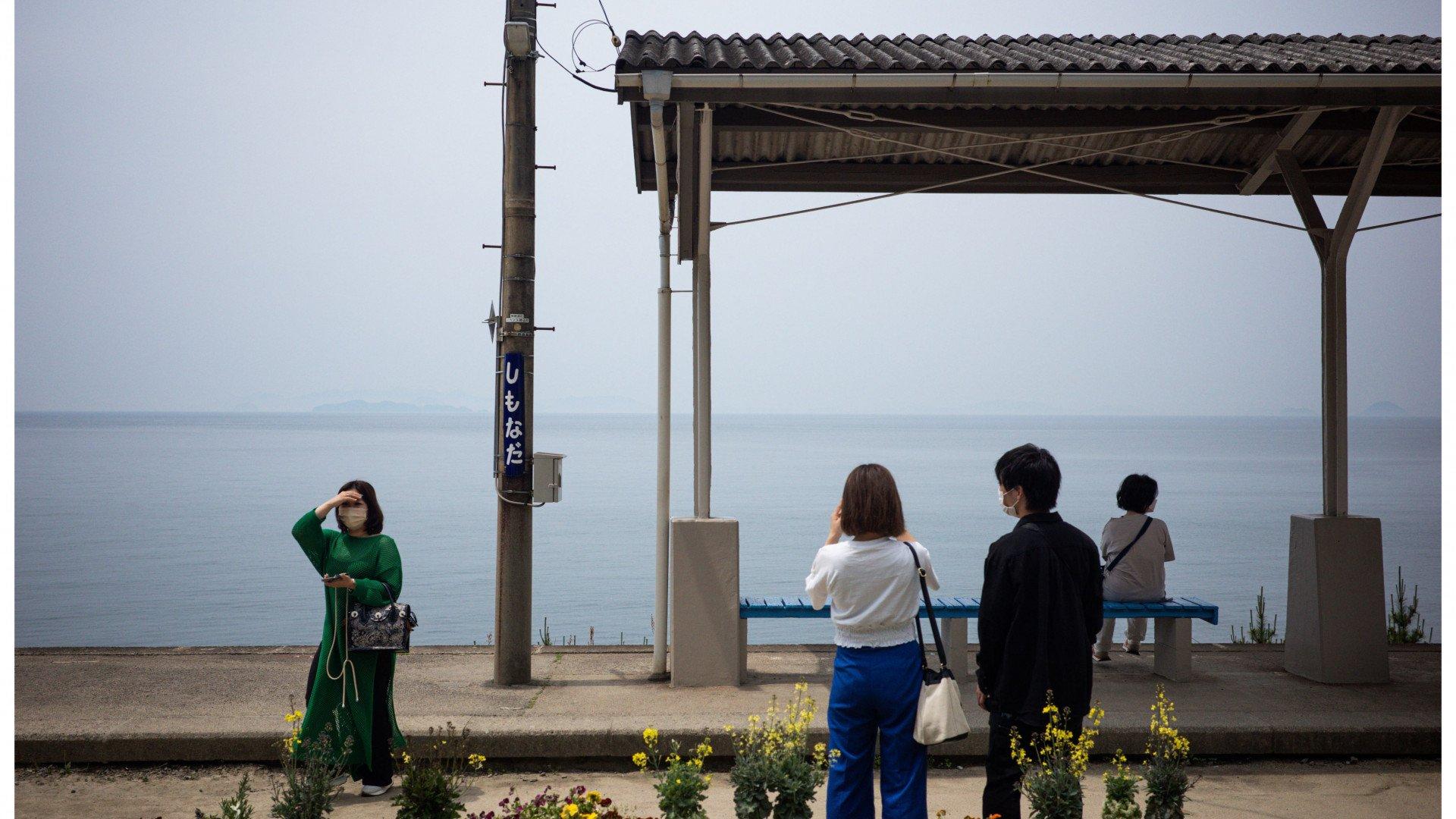 People at coastal train station platform overlooking calm sea in Japan