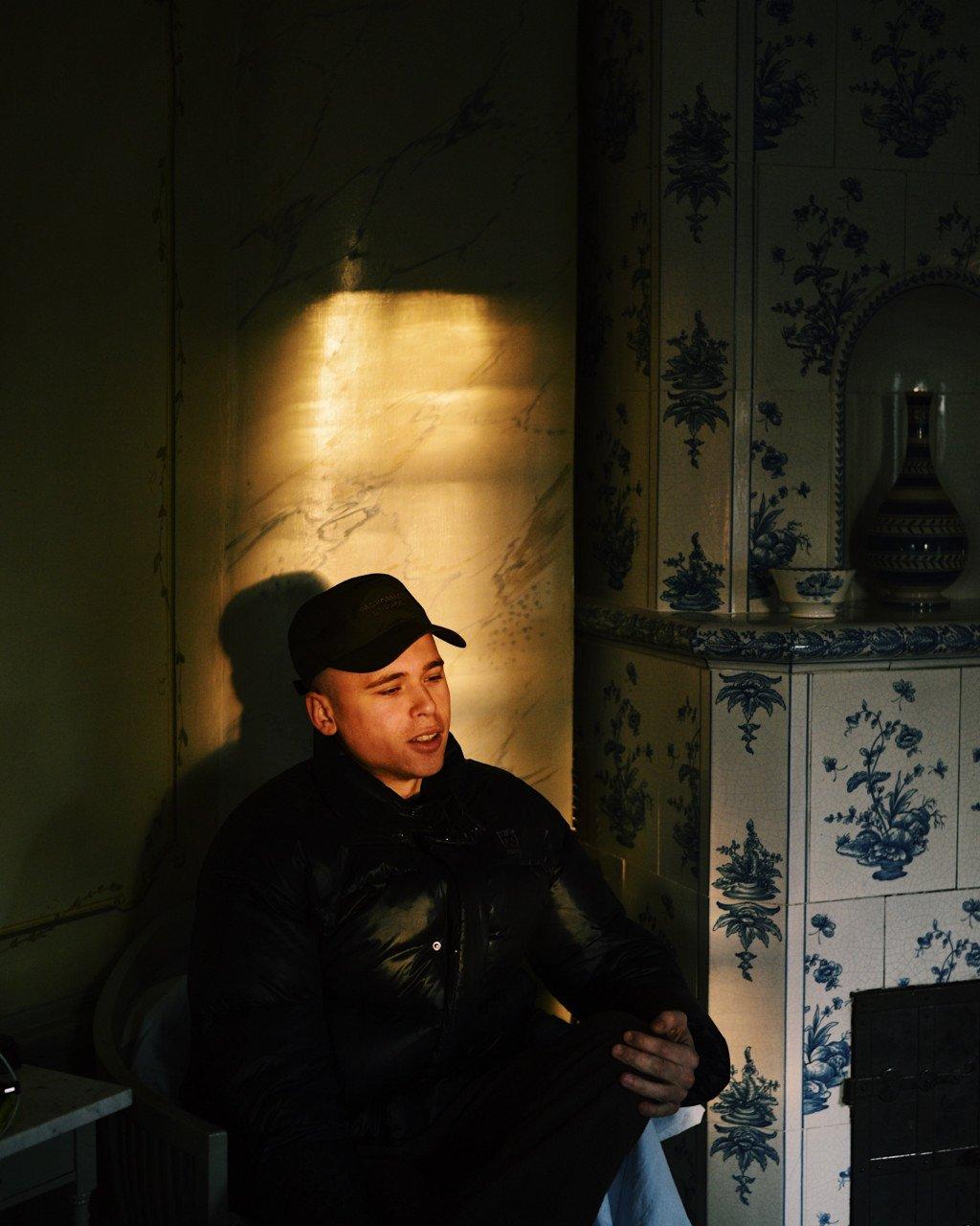 Model wearing black cycling cap and jacket in interior setting with blue ceramic tiles
