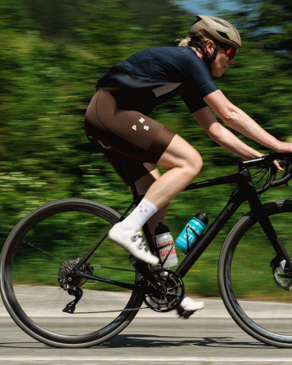 Model wearing navy jersey and brown shorts on time trial bike in motion