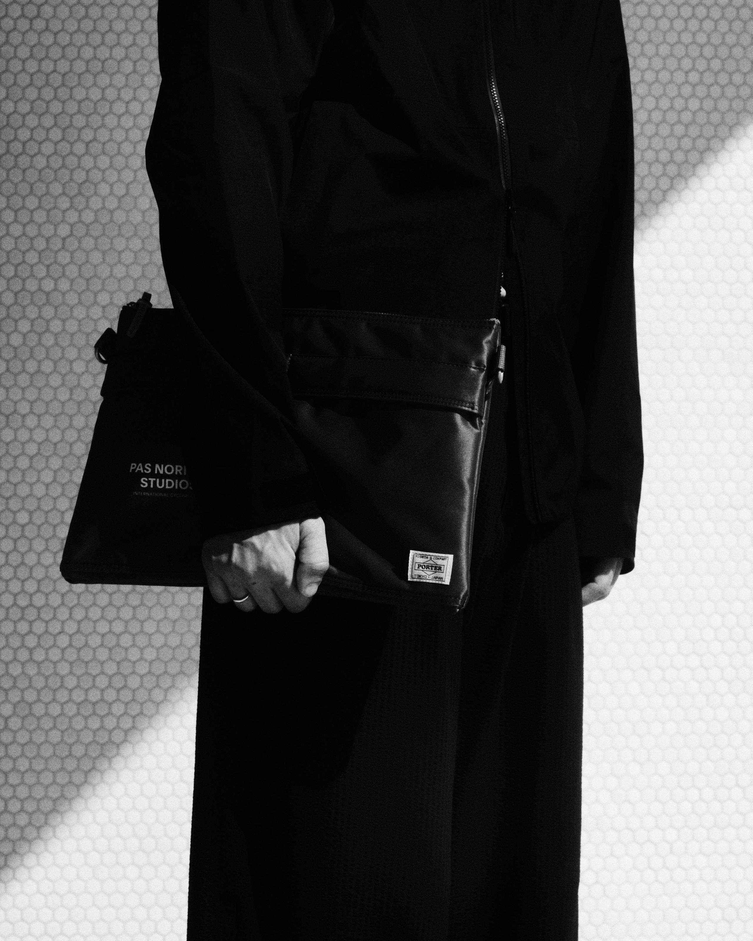 Model wearing black outfit holding black Porter collaboration bag with logo branding