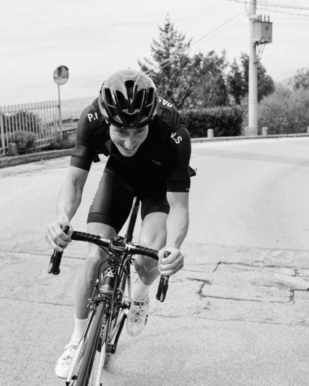 Model wearing black cycling kit in aerodynamic position on time trial bike, black and white photo