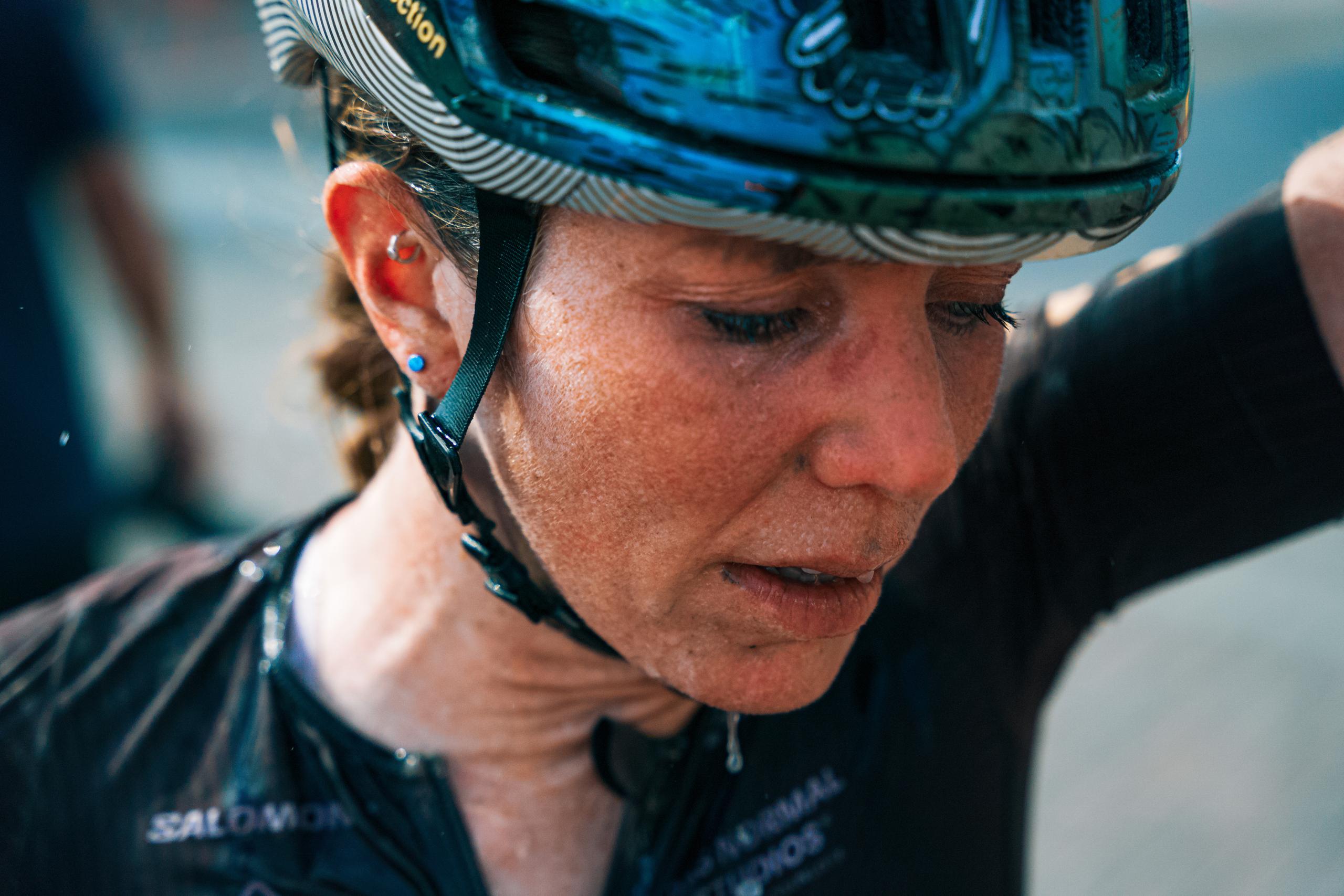 Model wearing blue and black patterned cycling helmet, adjusting chin strap
