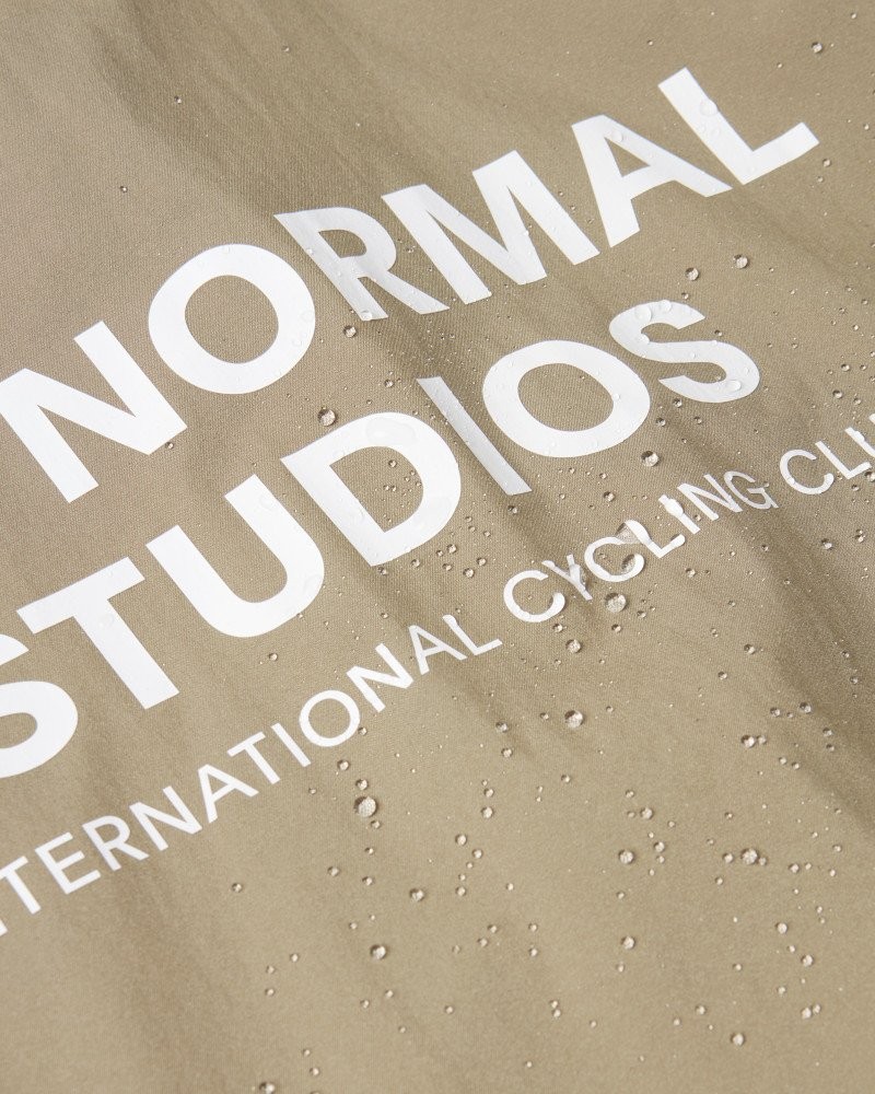 Beige Mechanism Stow Away jacket, detail view with white printed logo and water droplets