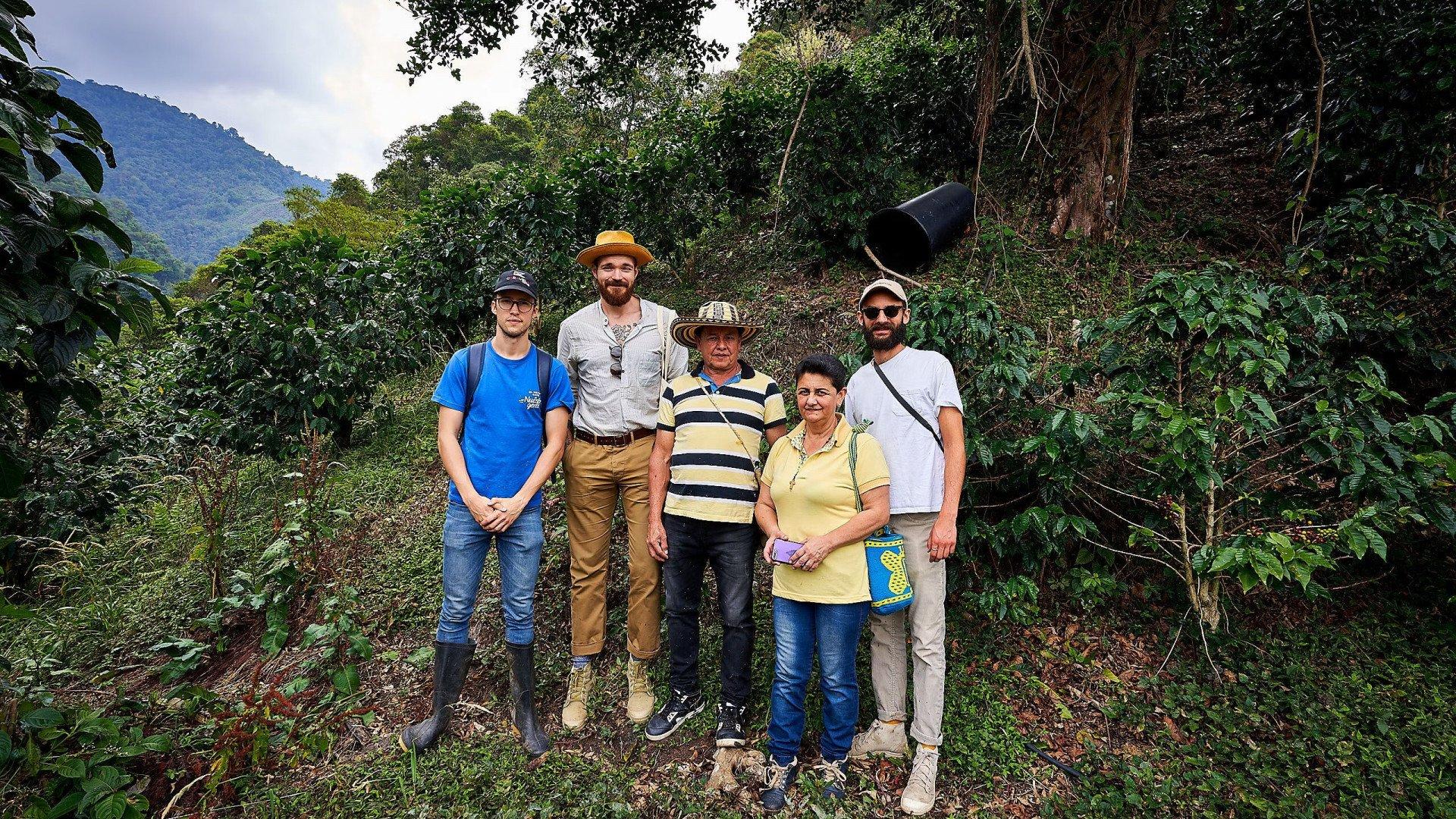 Group of five people standing together on coffee farm in lush mountain landscape