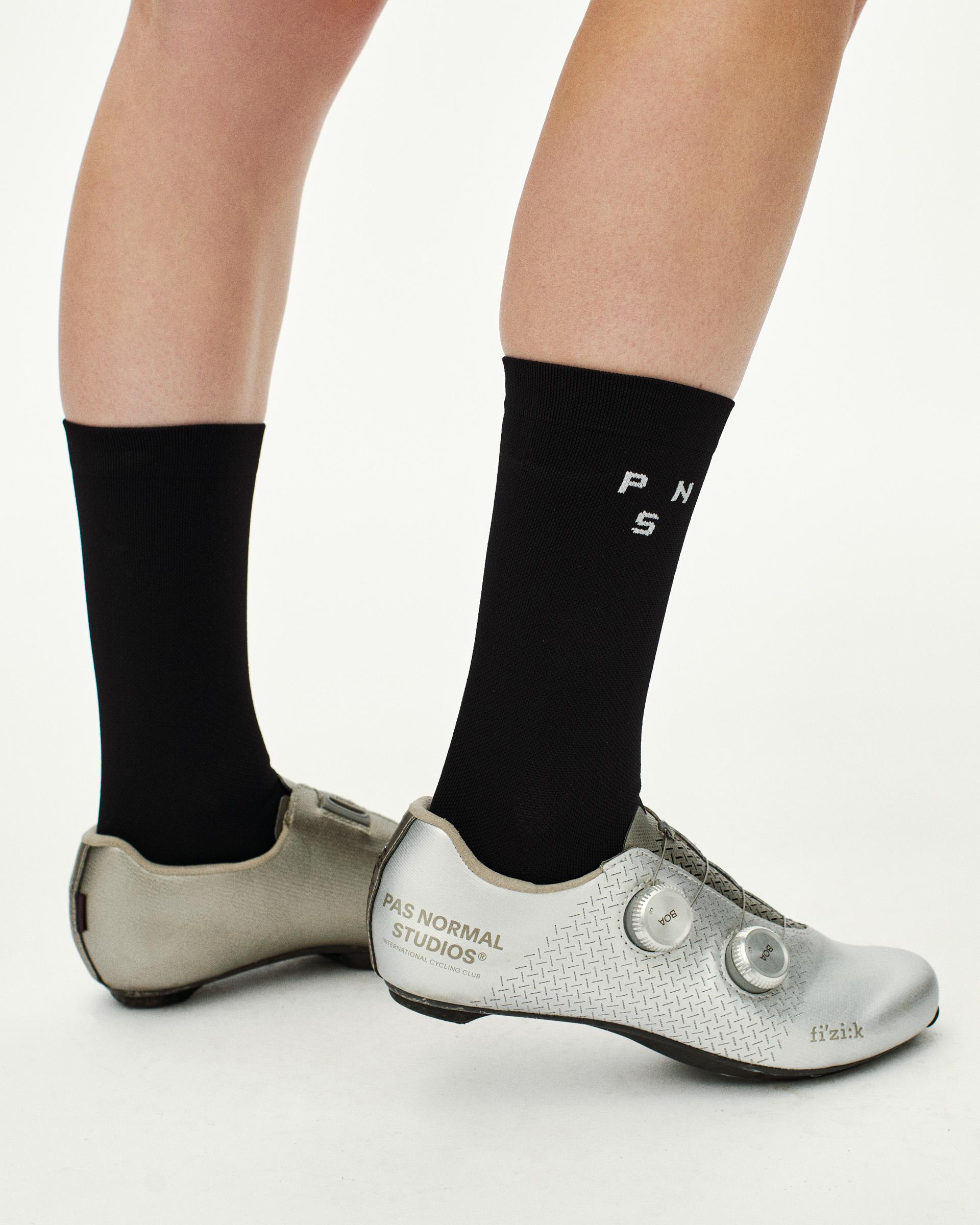 Black Essential cycling socks on model with white PNS logo detail