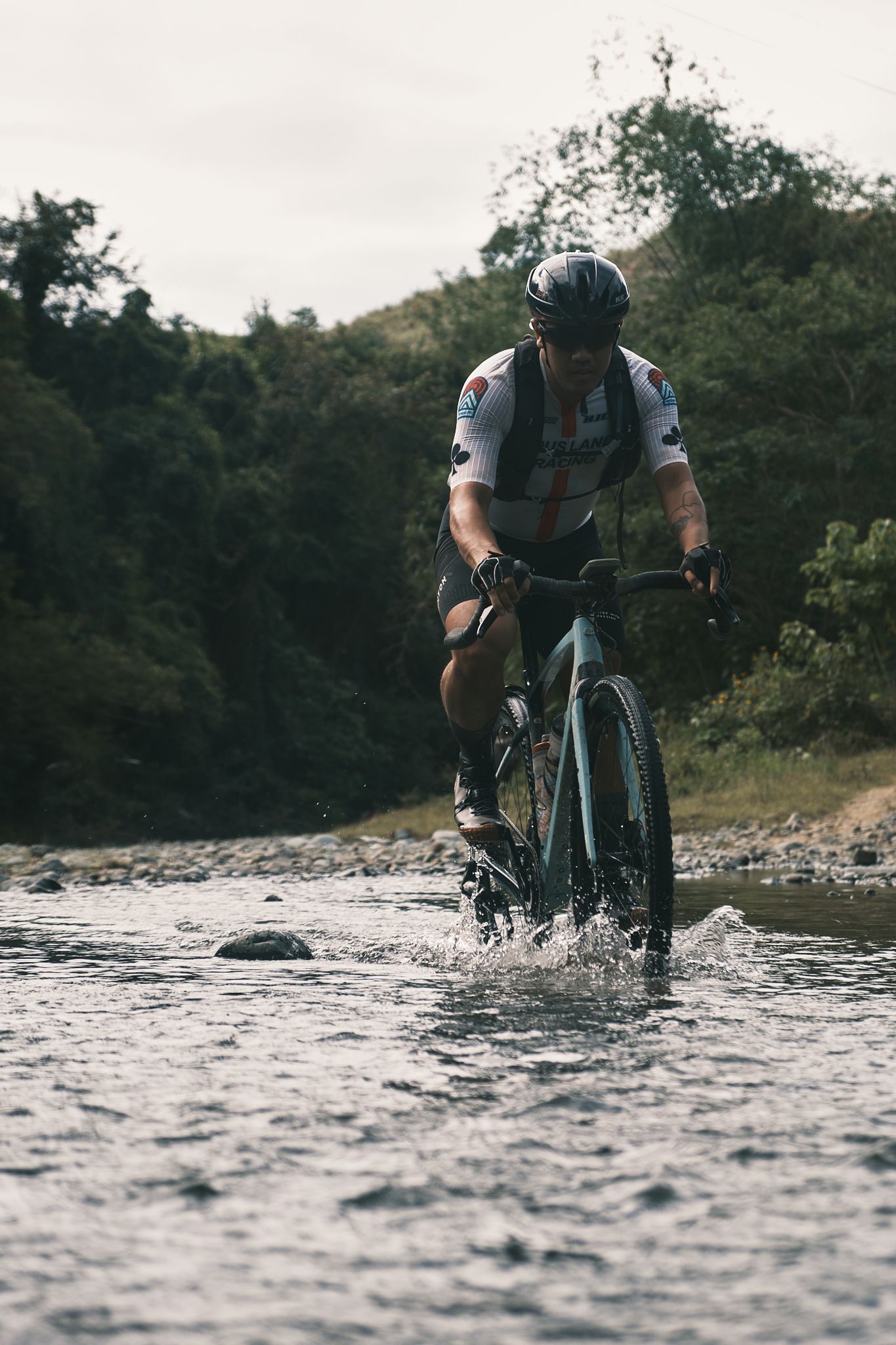 Cyclist riding through stream wearing white jersey with geometric pattern and black bib shorts