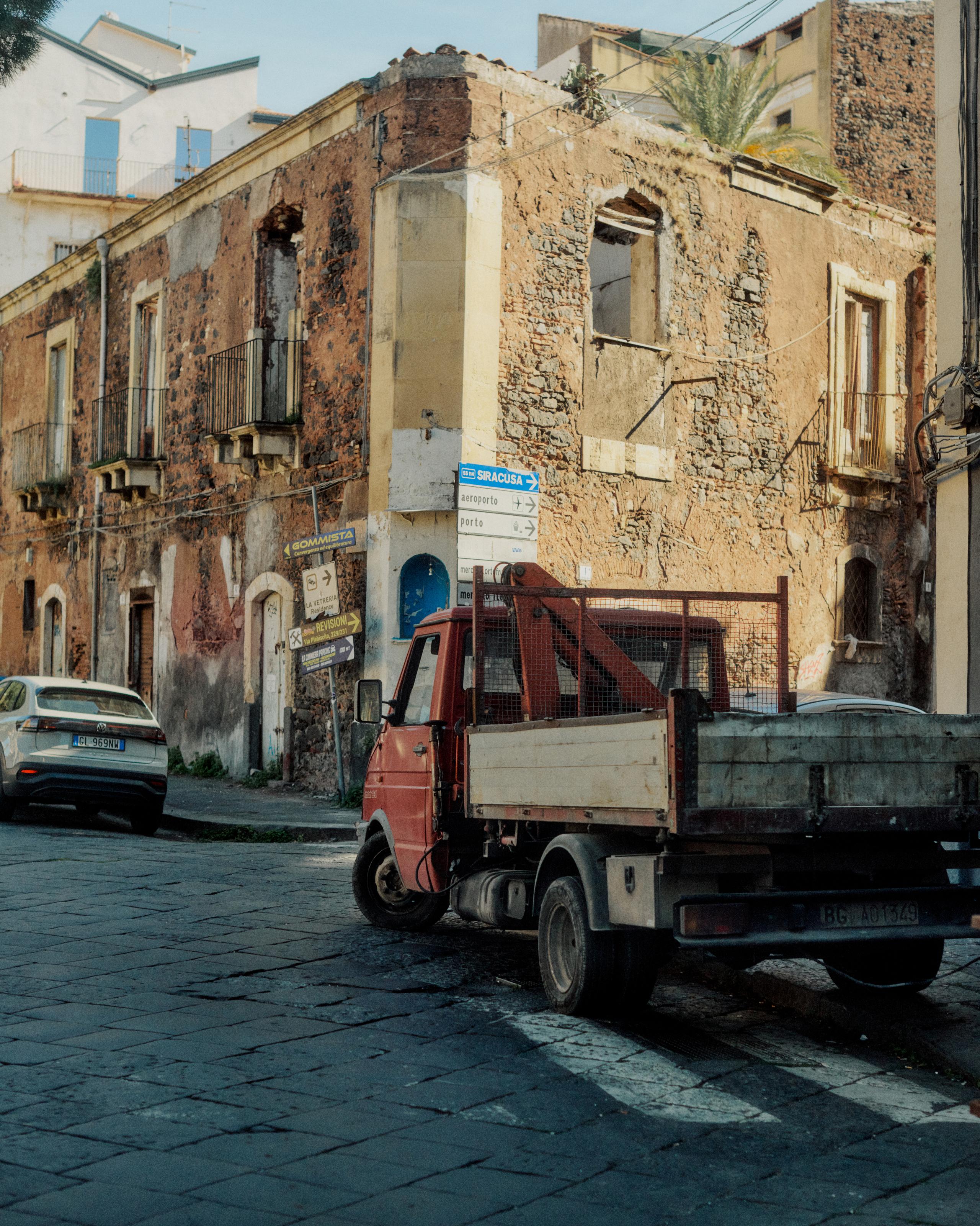 Historic weathered buildings and small truck on cobblestone street in Sicily