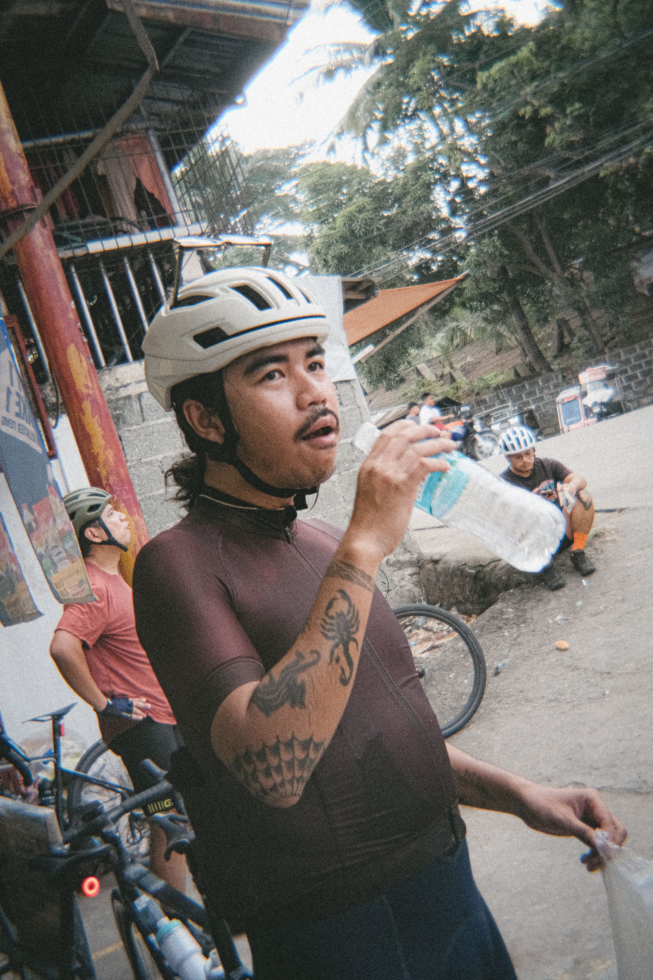 Cyclist drinking water while wearing dark purple jersey and white helmet during outdoor ride break