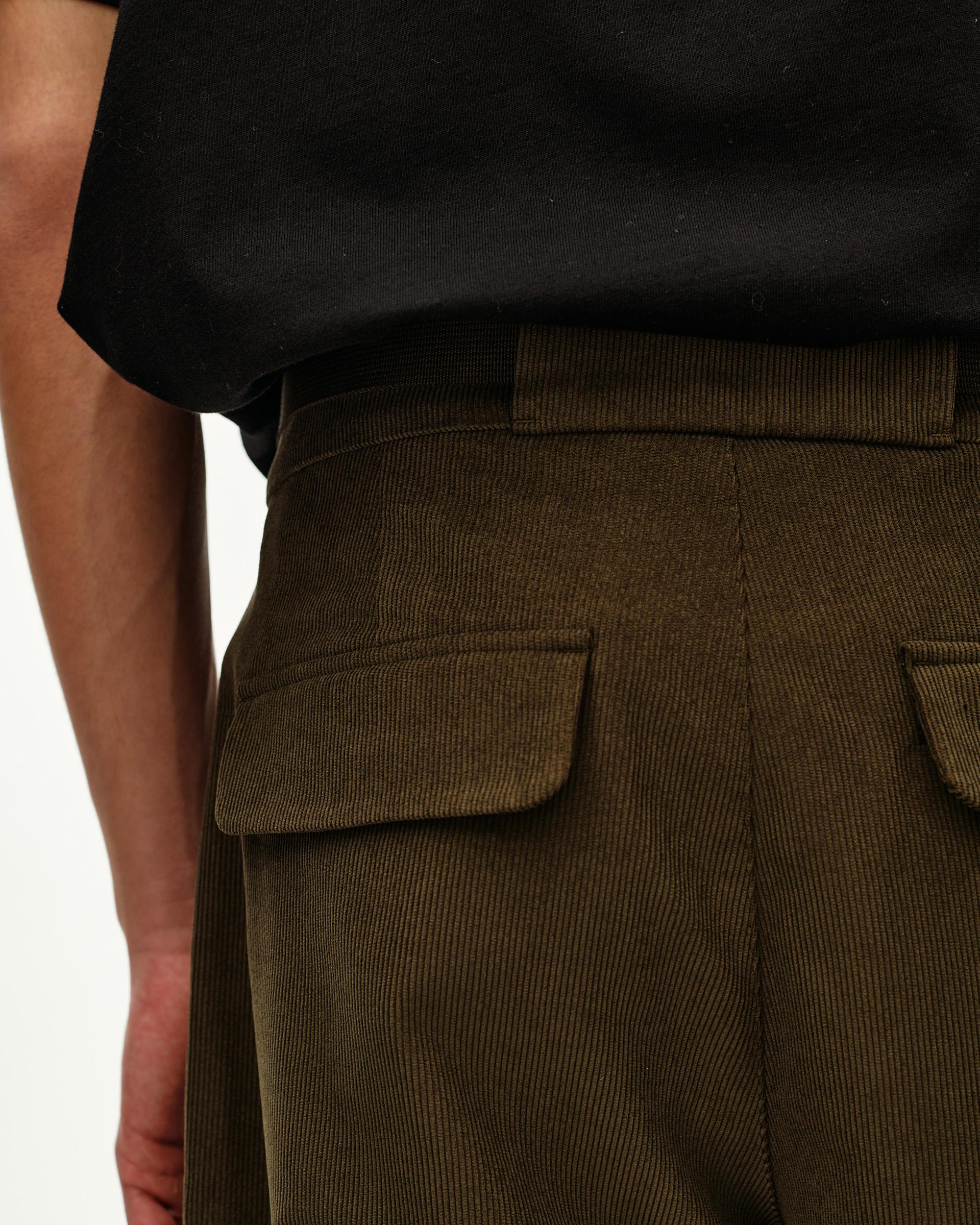 Deep Olive Off-Race Corduroy pants, detail view on model showing flap pockets and ribbed waistband