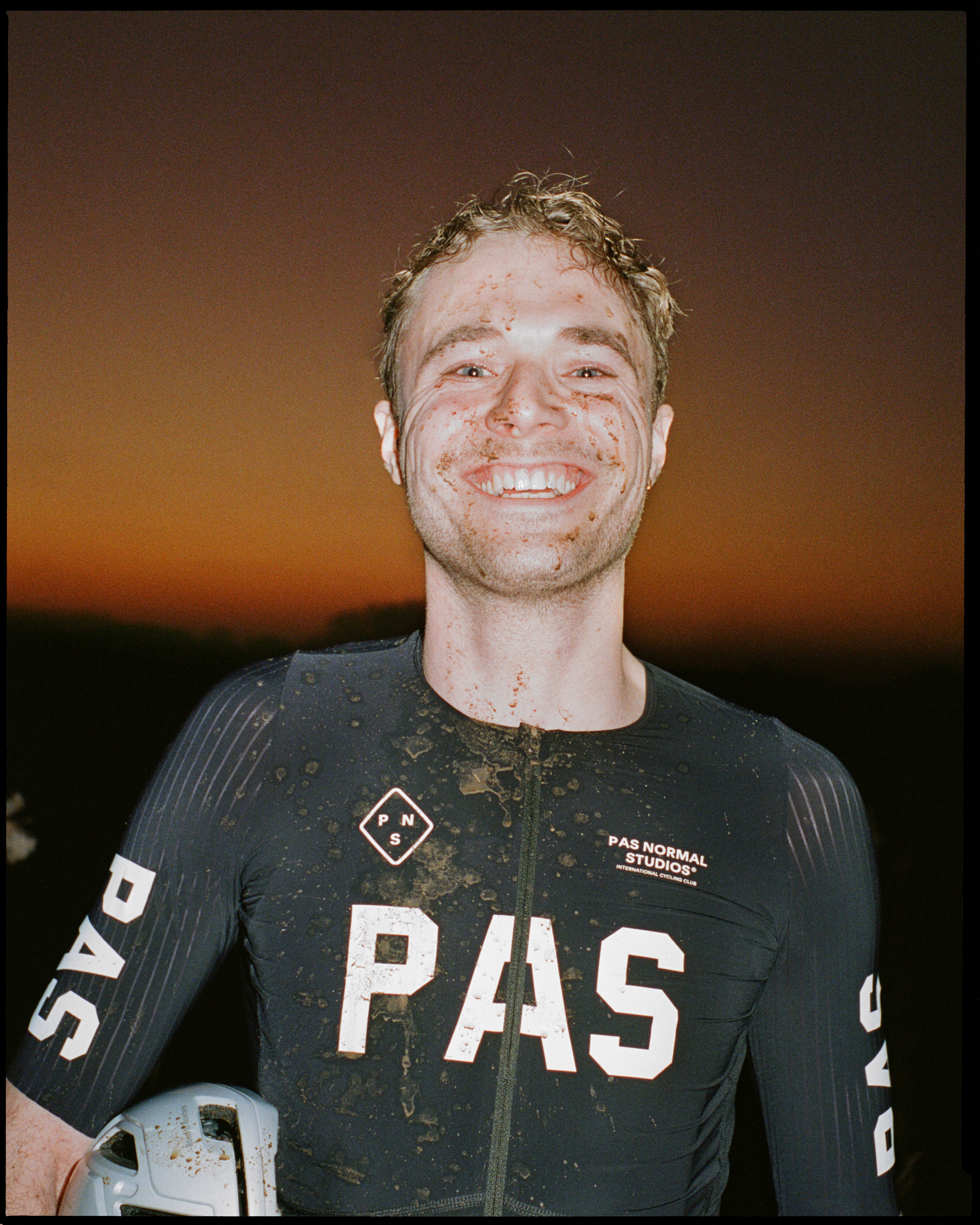 Model wearing Men's PAS Jersey in dark grey with white lettering, mud-covered after cycling