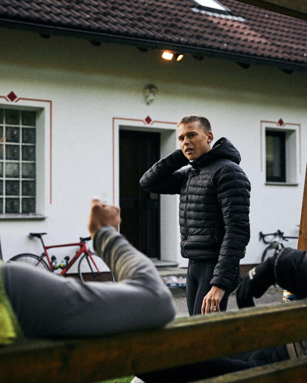 Model wearing black quilted down jacket with hood in courtyard setting with bicycles