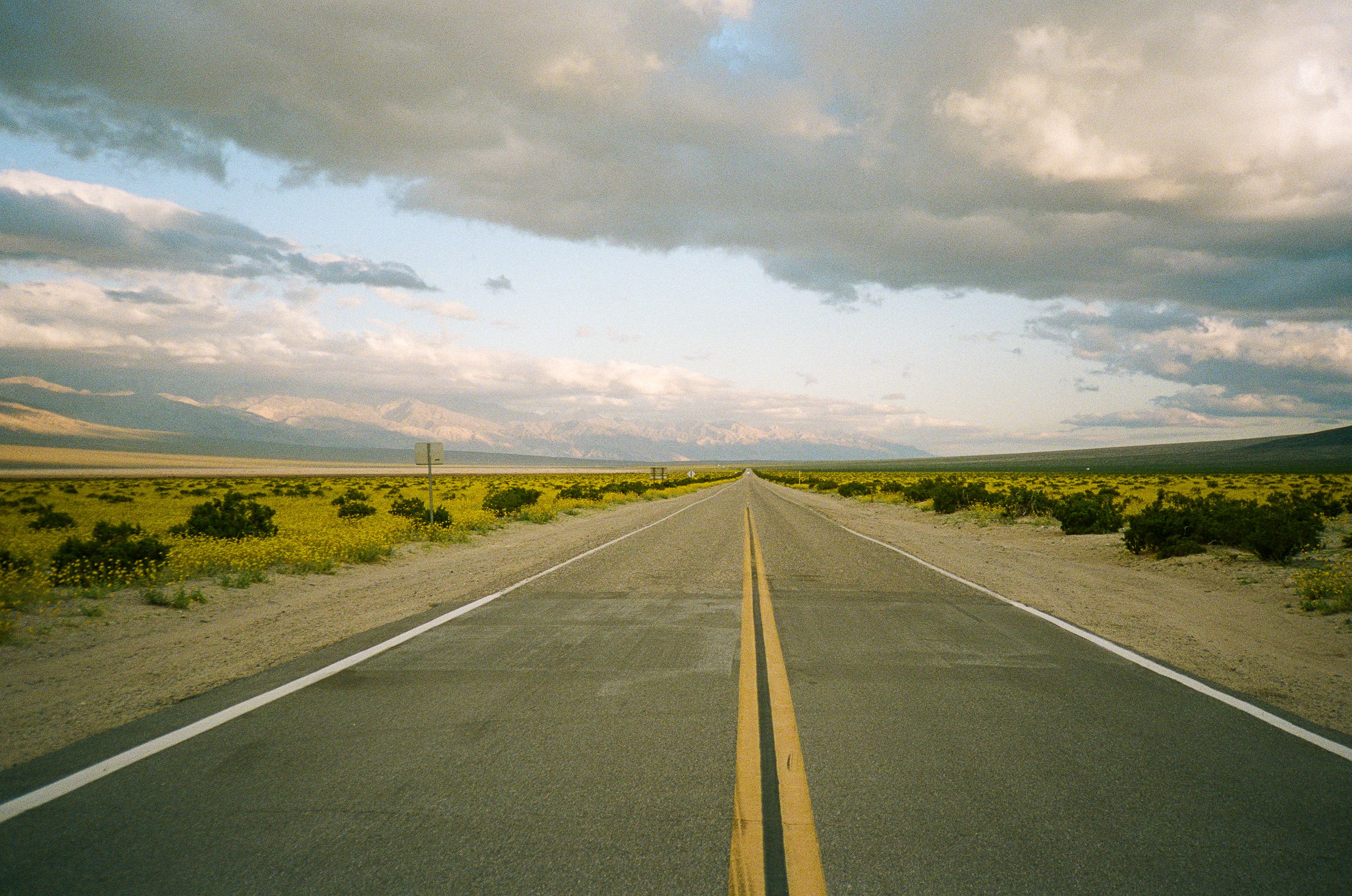 Empty desert highway stretching toward mountains under dramatic cloudy sky in Death Valley