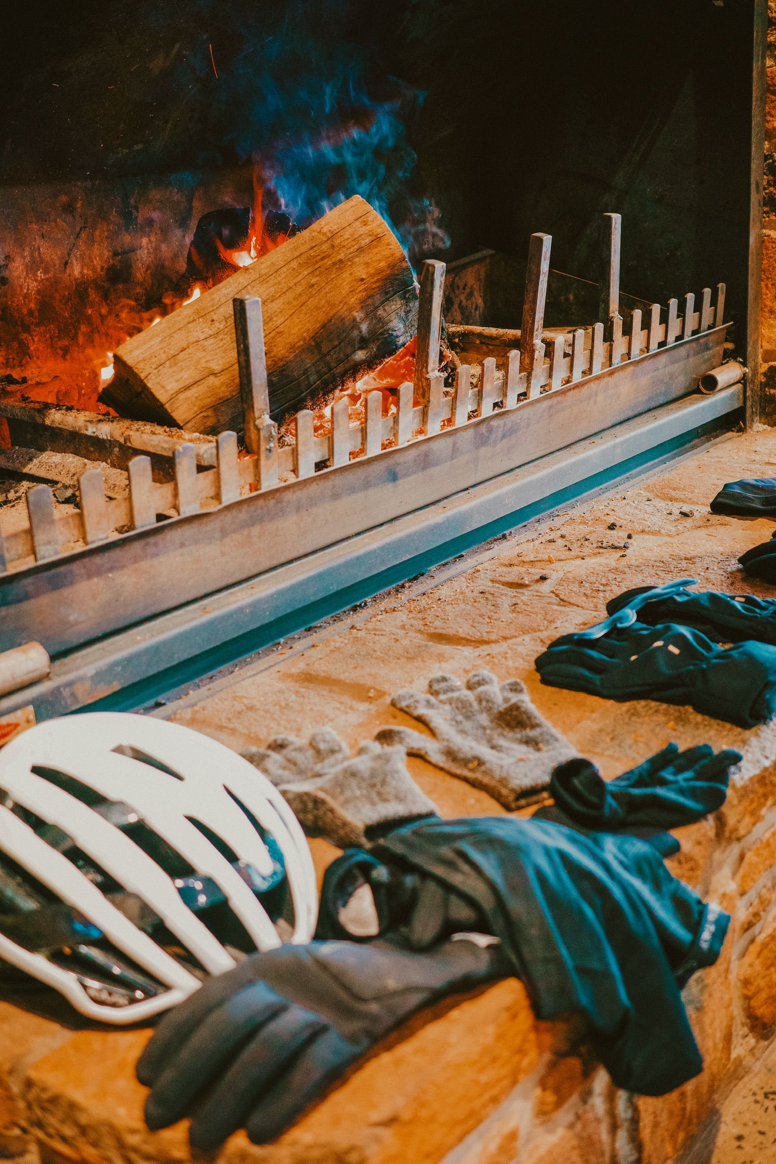 Cycling gear including helmet and gloves arranged by fireplace with burning logs
