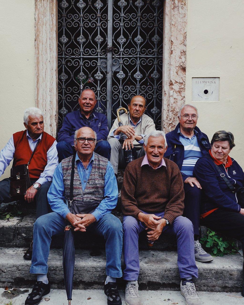 Group of elderly Italian men sitting together outside ornate doorway