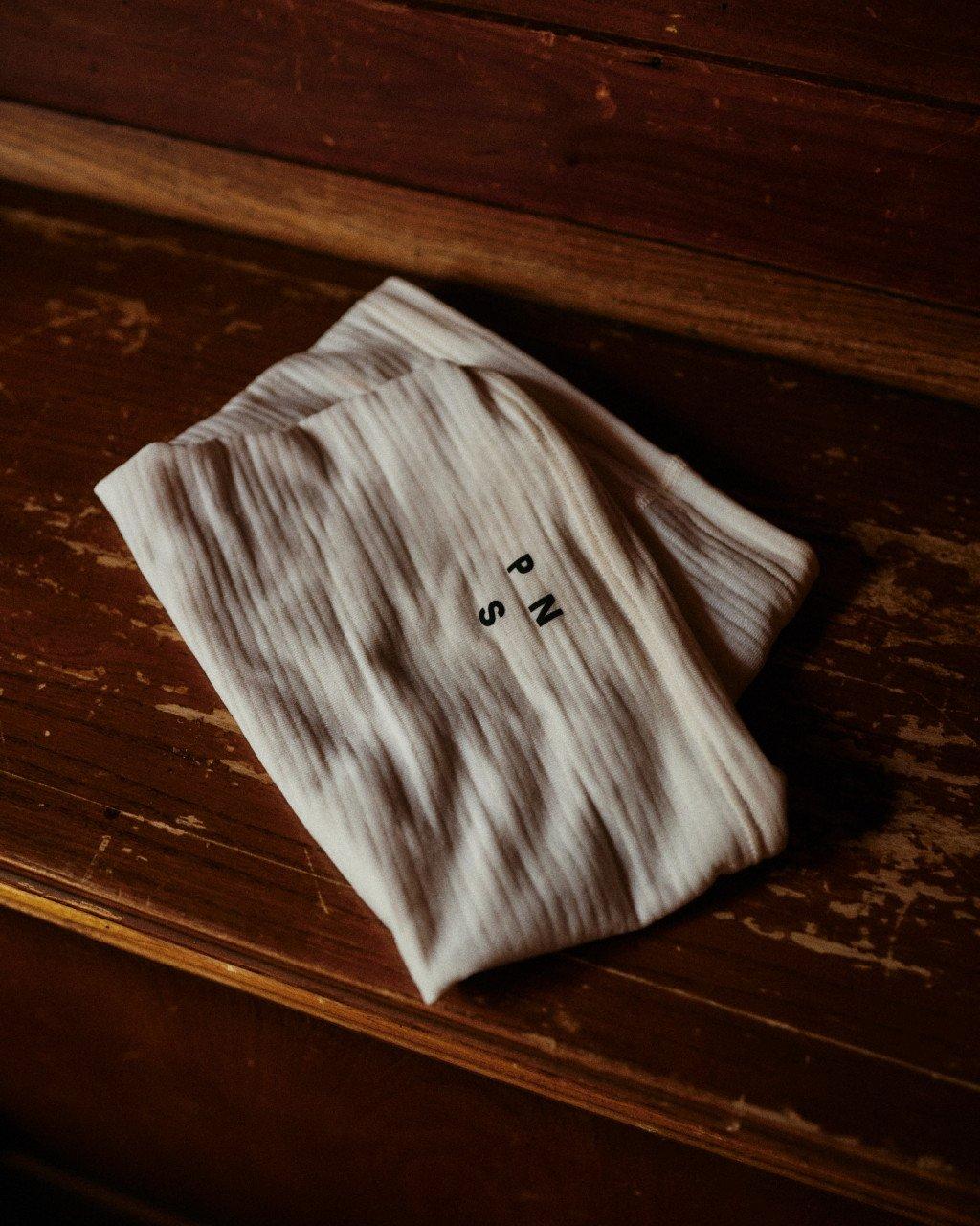 Cream ribbed knit garment with small lettering folded on wooden surface