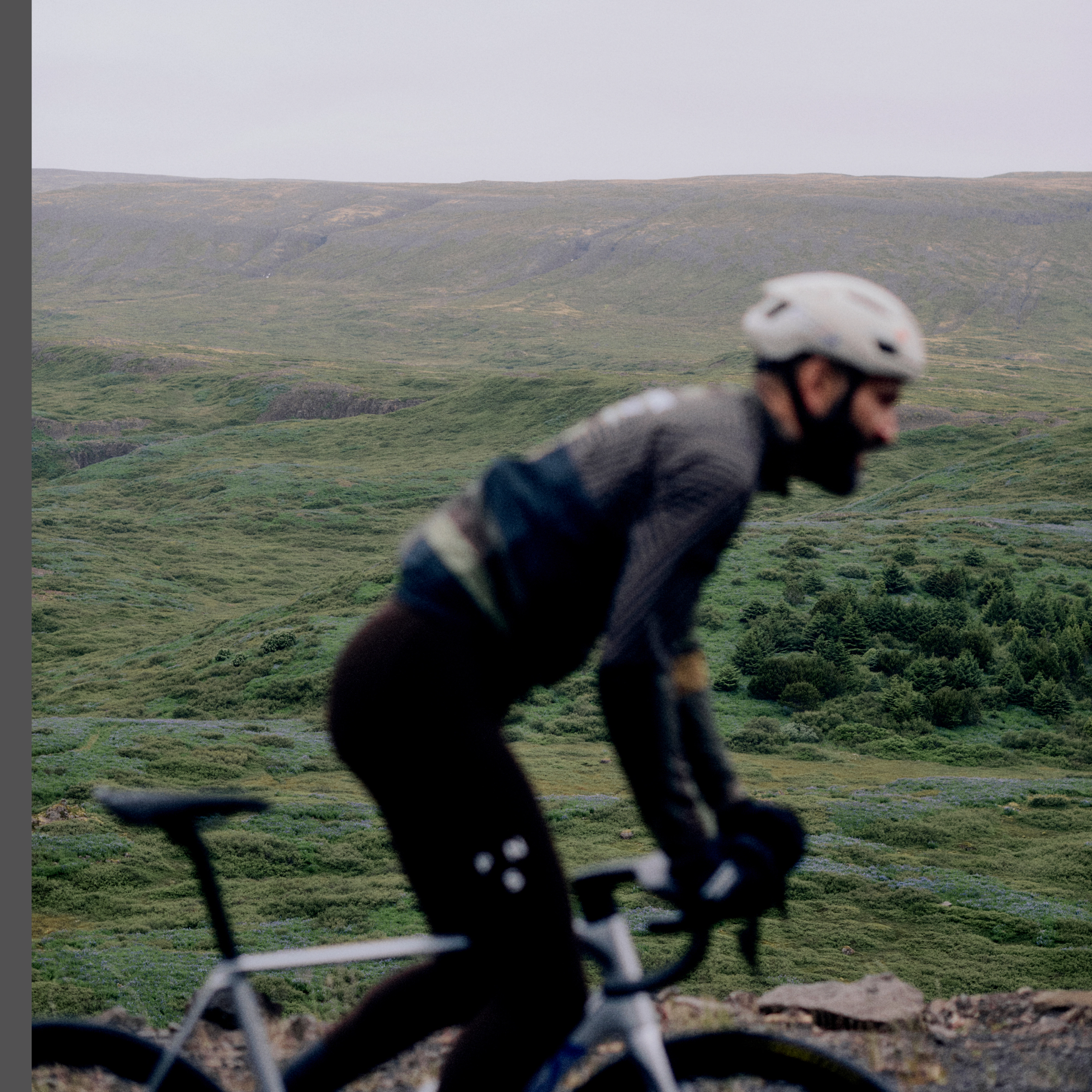 Black Mechanism Thermal Long Sleeve cycling jersey on model, side view worn while riding in hilly landscape