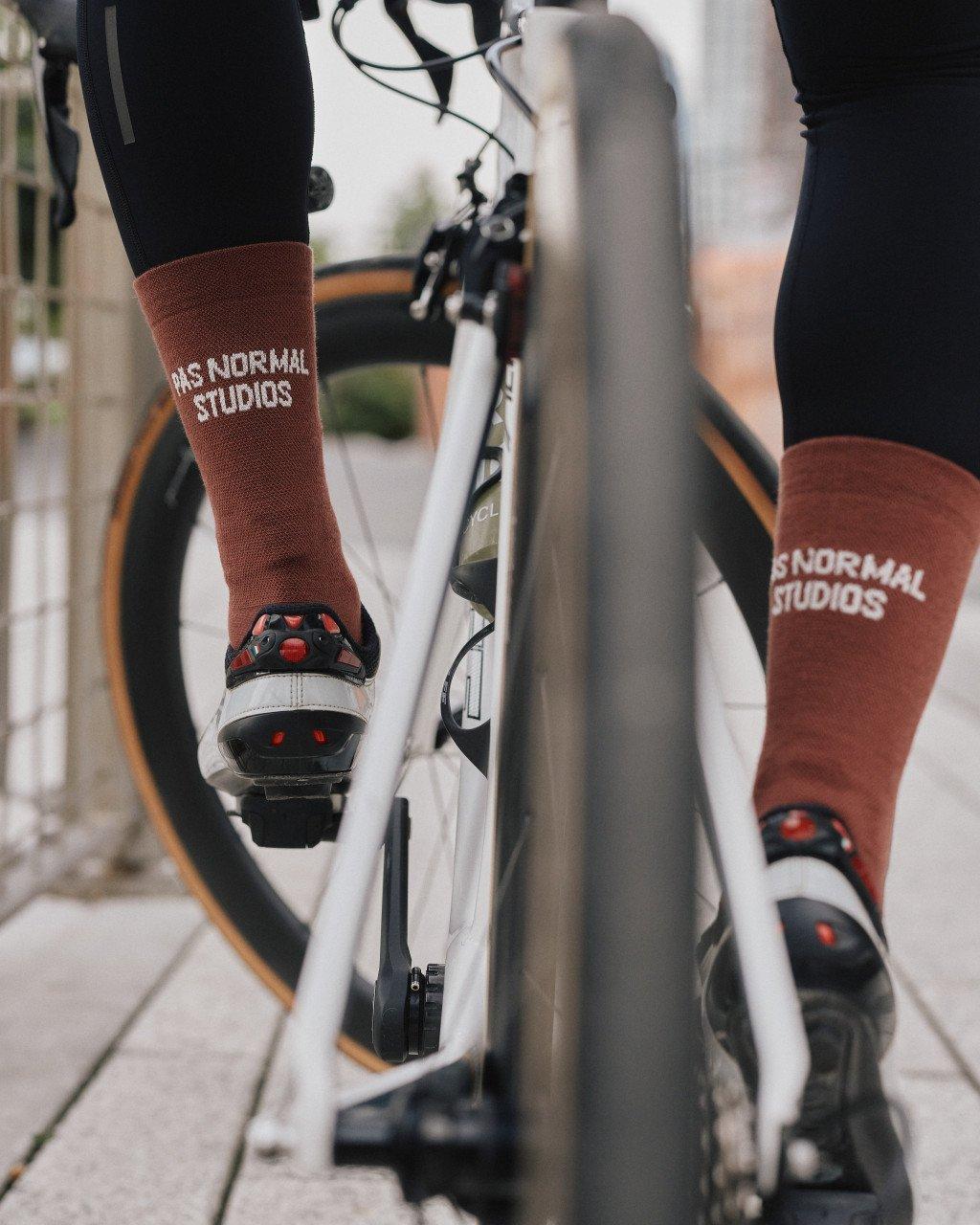 Brown cycling socks with white branding on cyclist's feet positioned on bike pedals