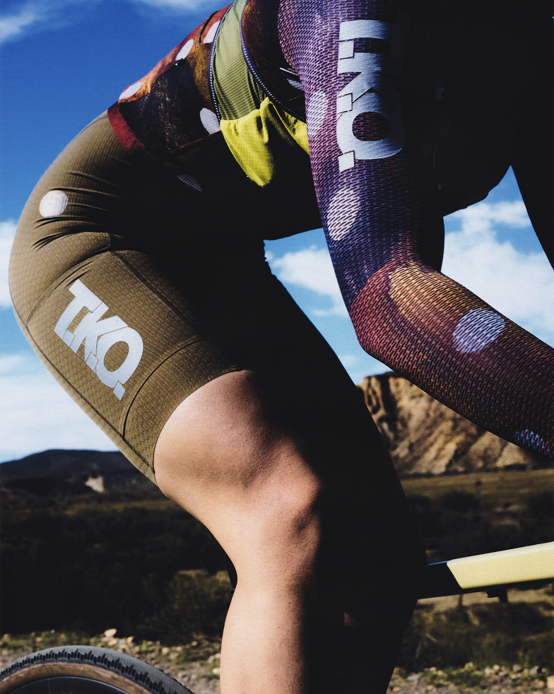 Model wearing multicolored cycling kit with geometric pattern jersey and olive shorts with leg branding outdoors