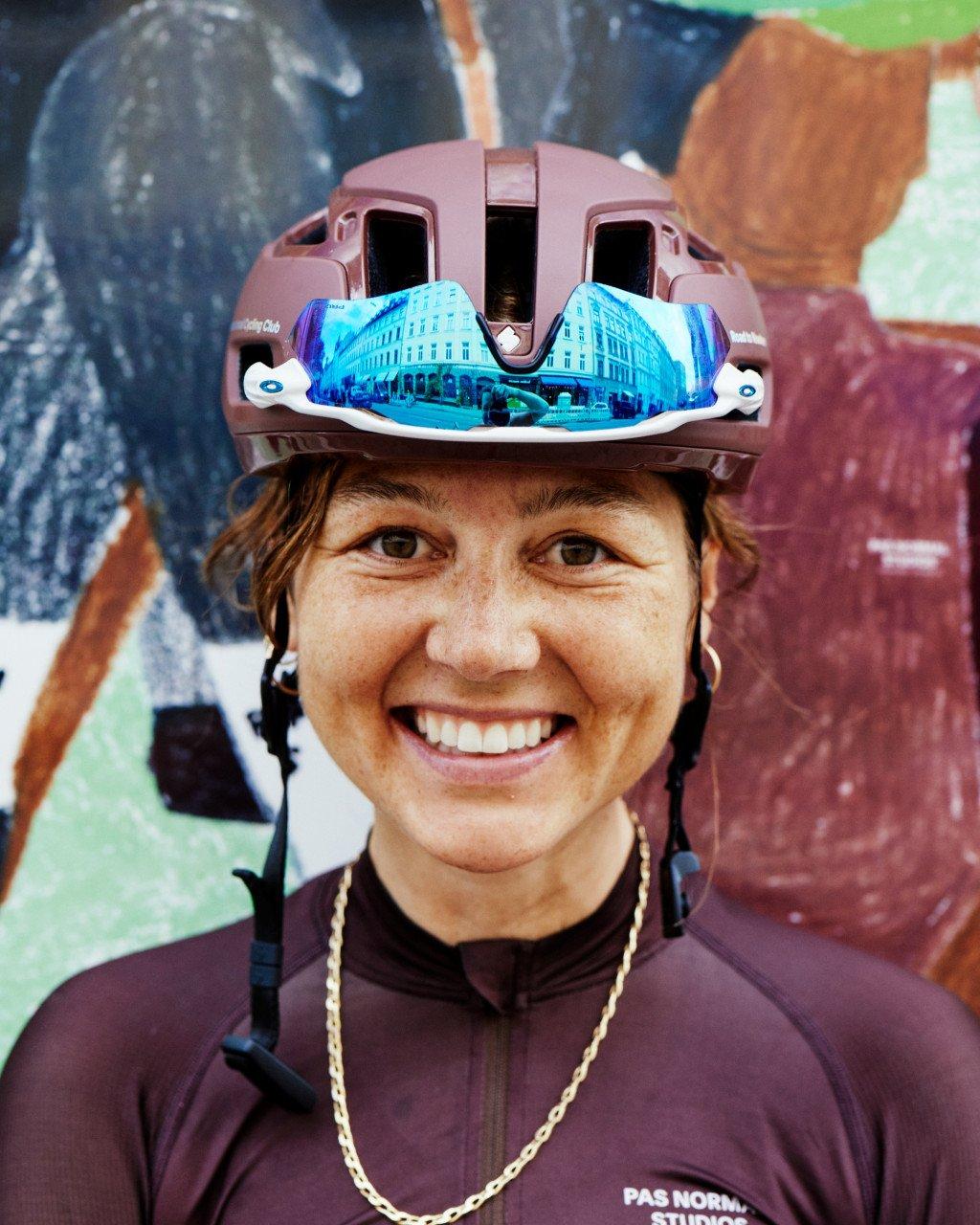 Model wearing purple cycling jersey with reflective sunglasses and helmet, smiling at camera