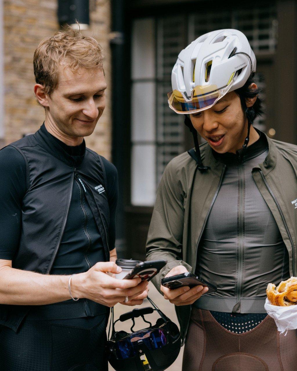 Male and female cyclists wearing dark jackets checking phones, woman with white helmet