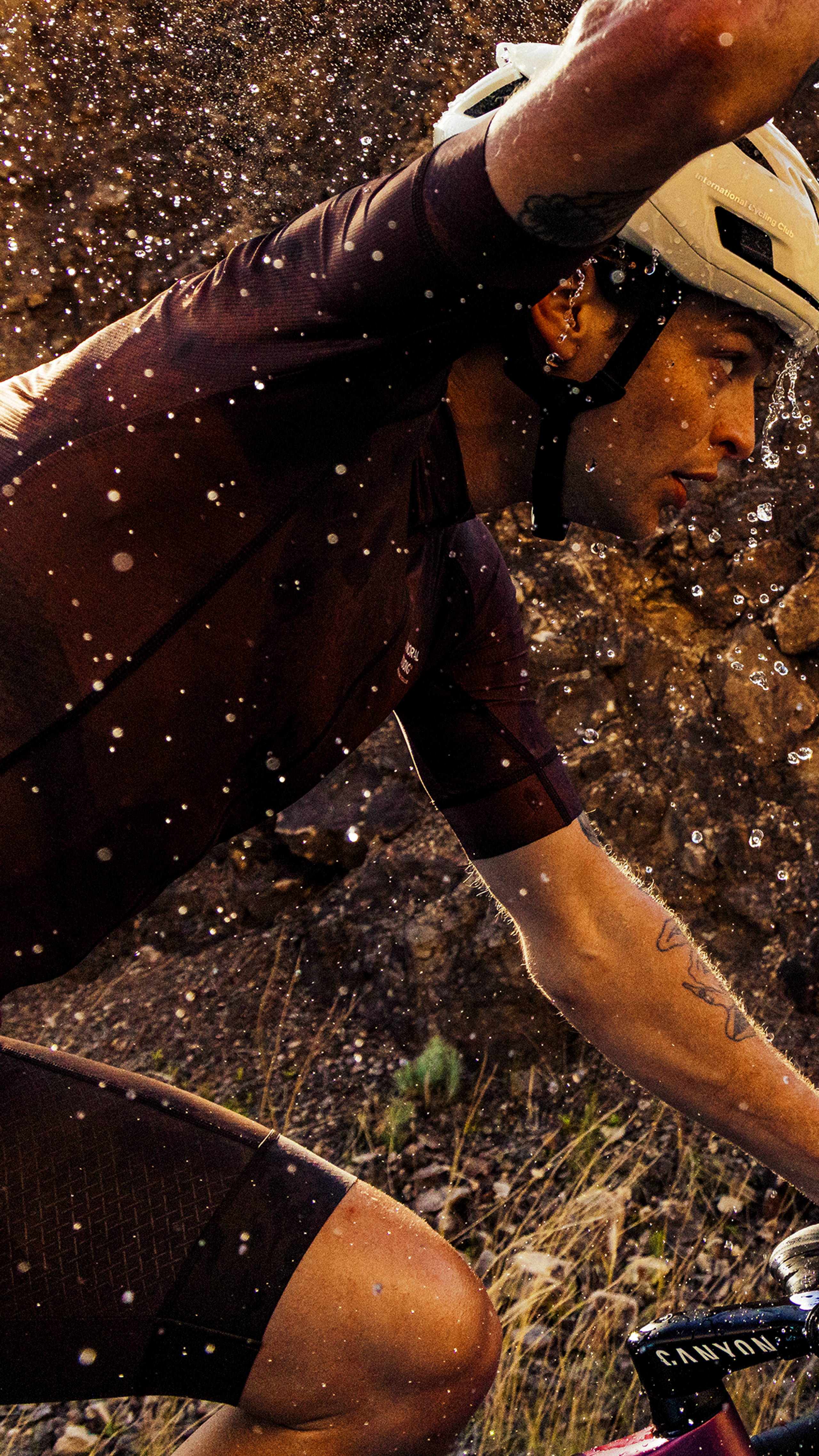 Model wearing dark cycling kit in wet conditions with water droplets and dramatic lighting