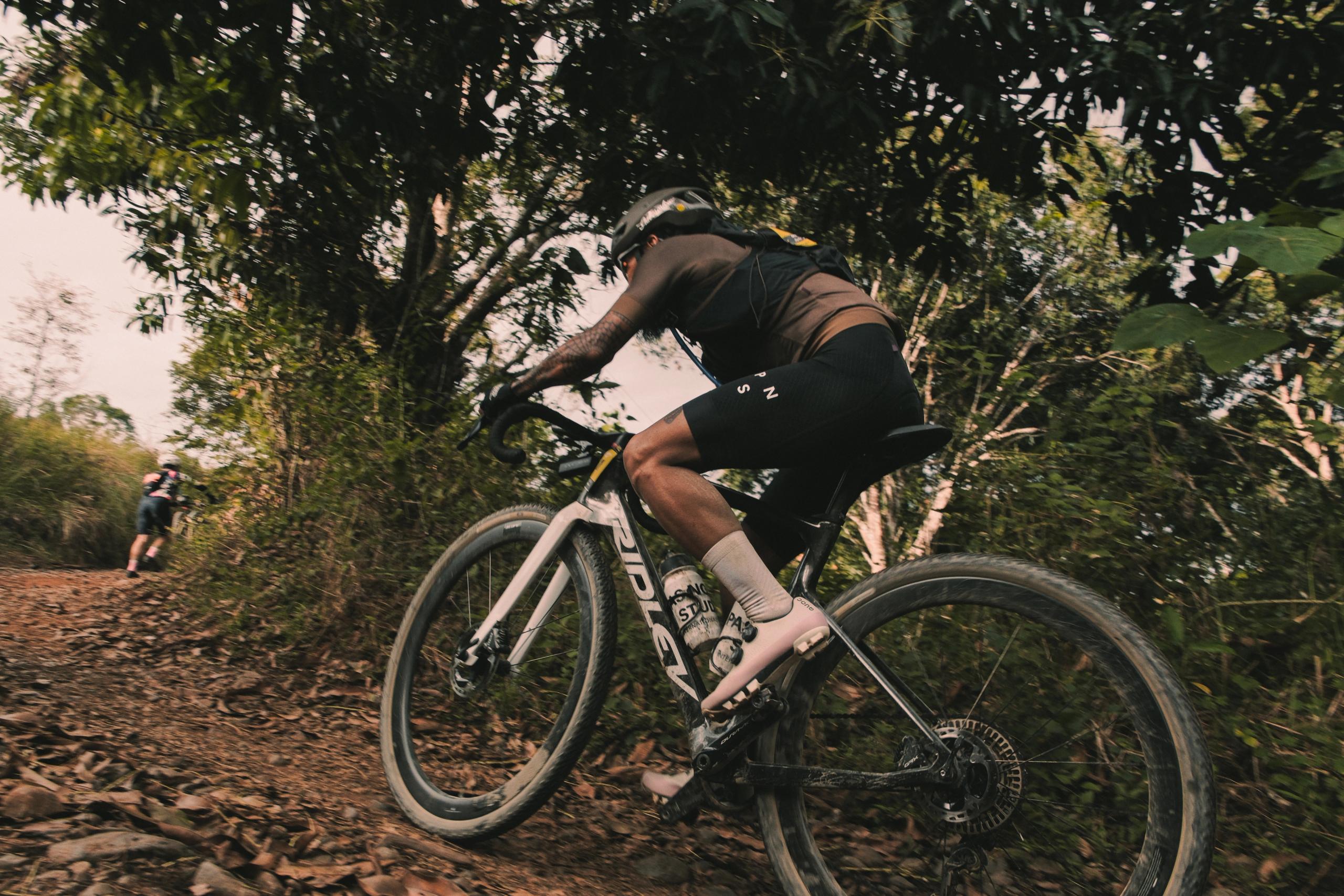 Cyclist in black kit racing on gravel bike through wooded trail in Philippines