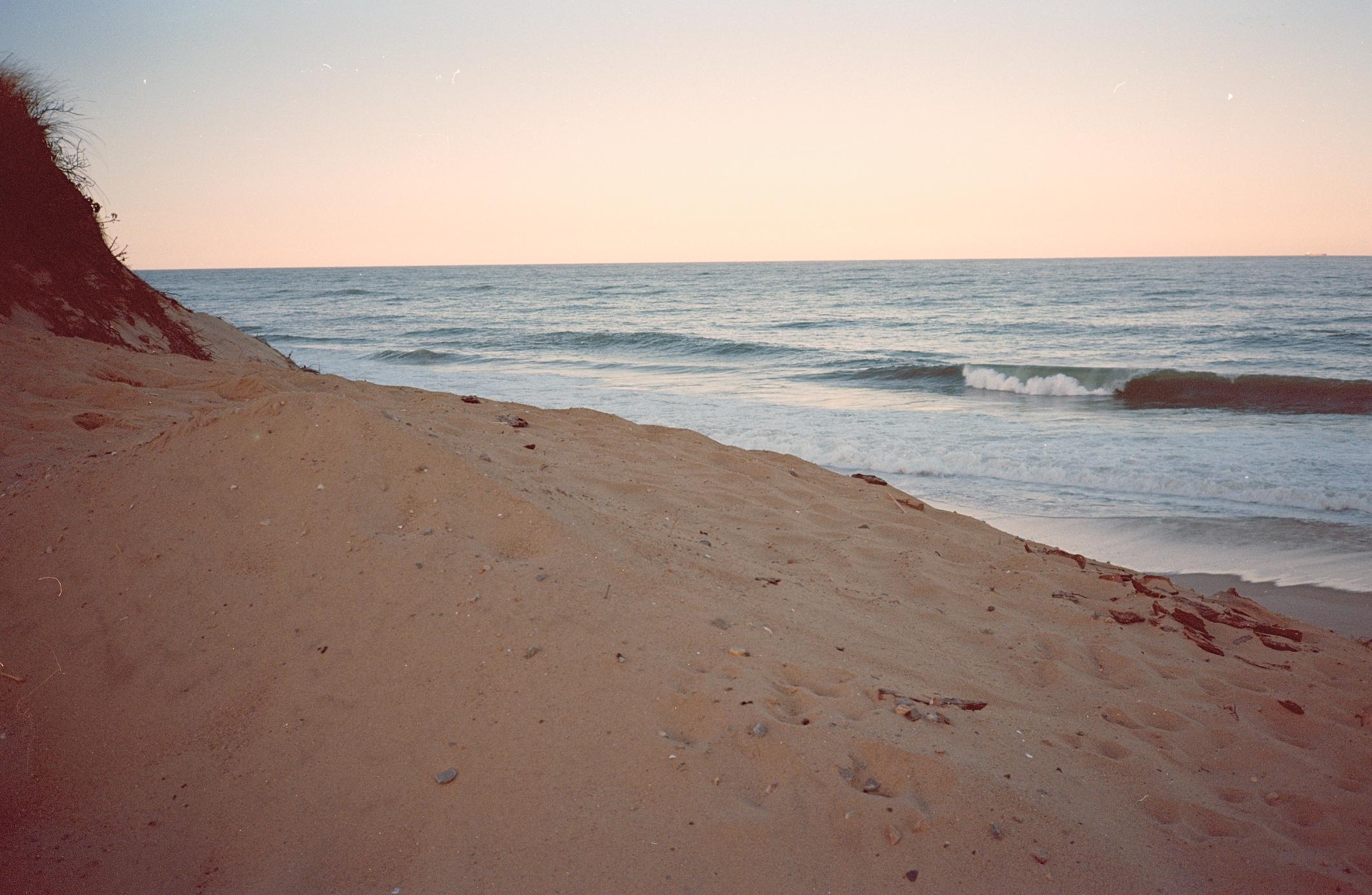 Coastal landscape with sandy beach and ocean waves at sunset