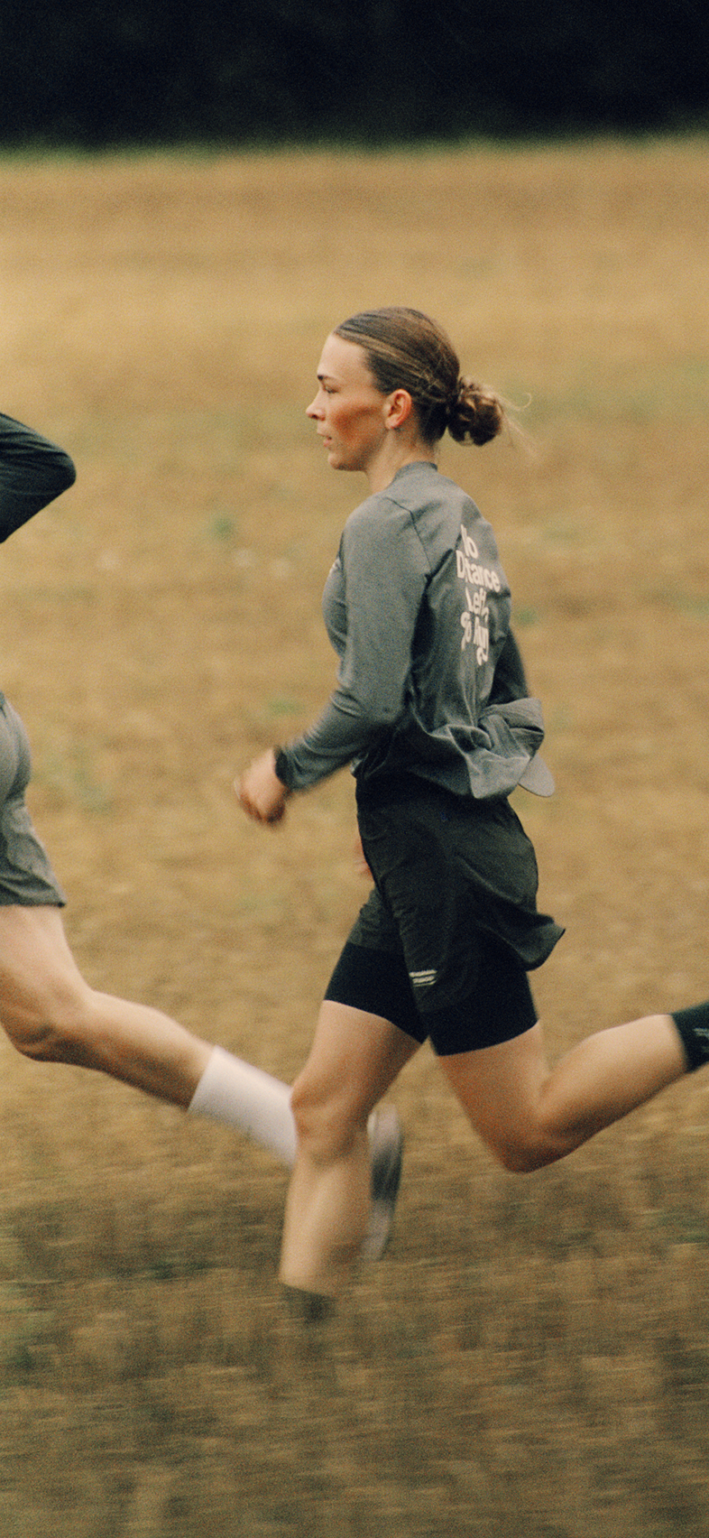 Model wearing grey long-sleeve shirt with back lettering and black shorts while running outdoors