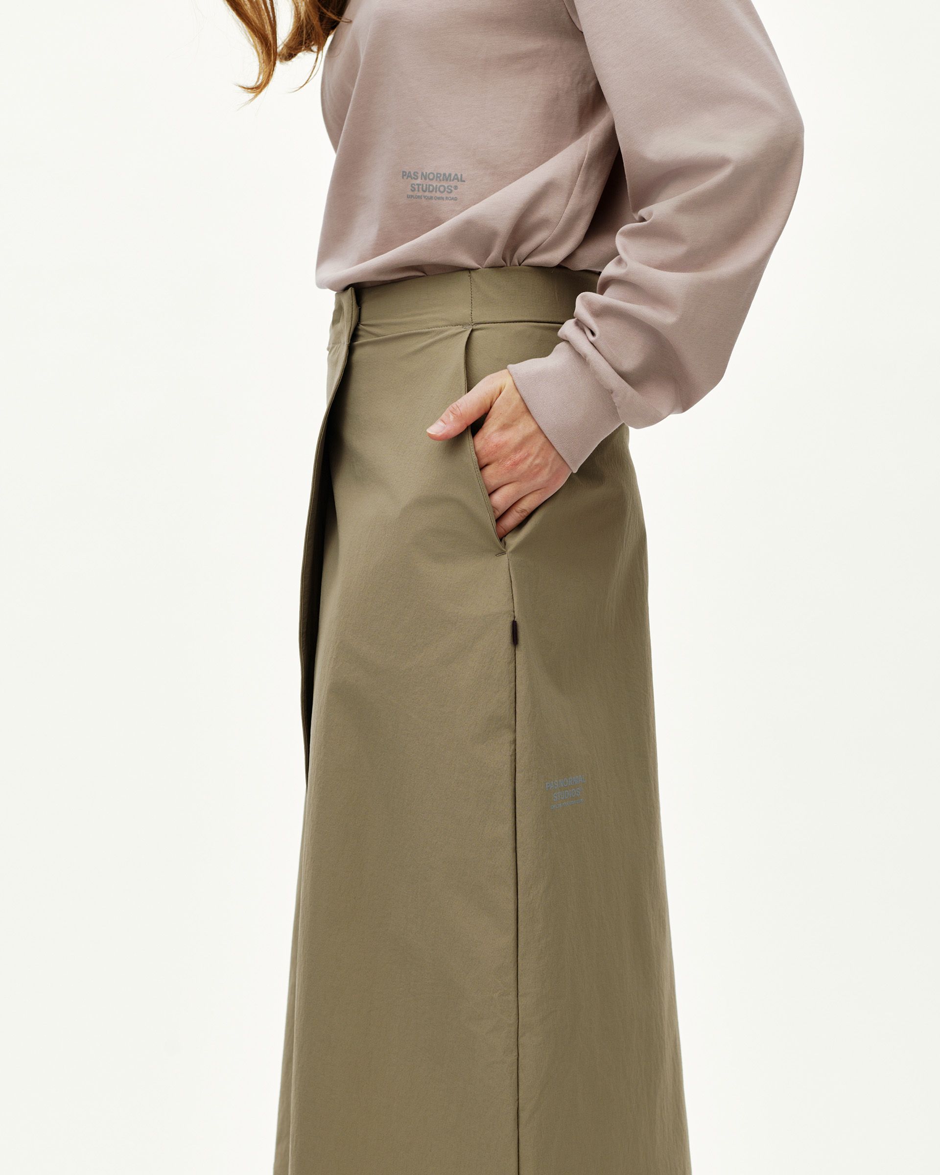 Dusty Earth khaki Off-Race women's tech skirt on model, side view with hand in pocket and back vent
