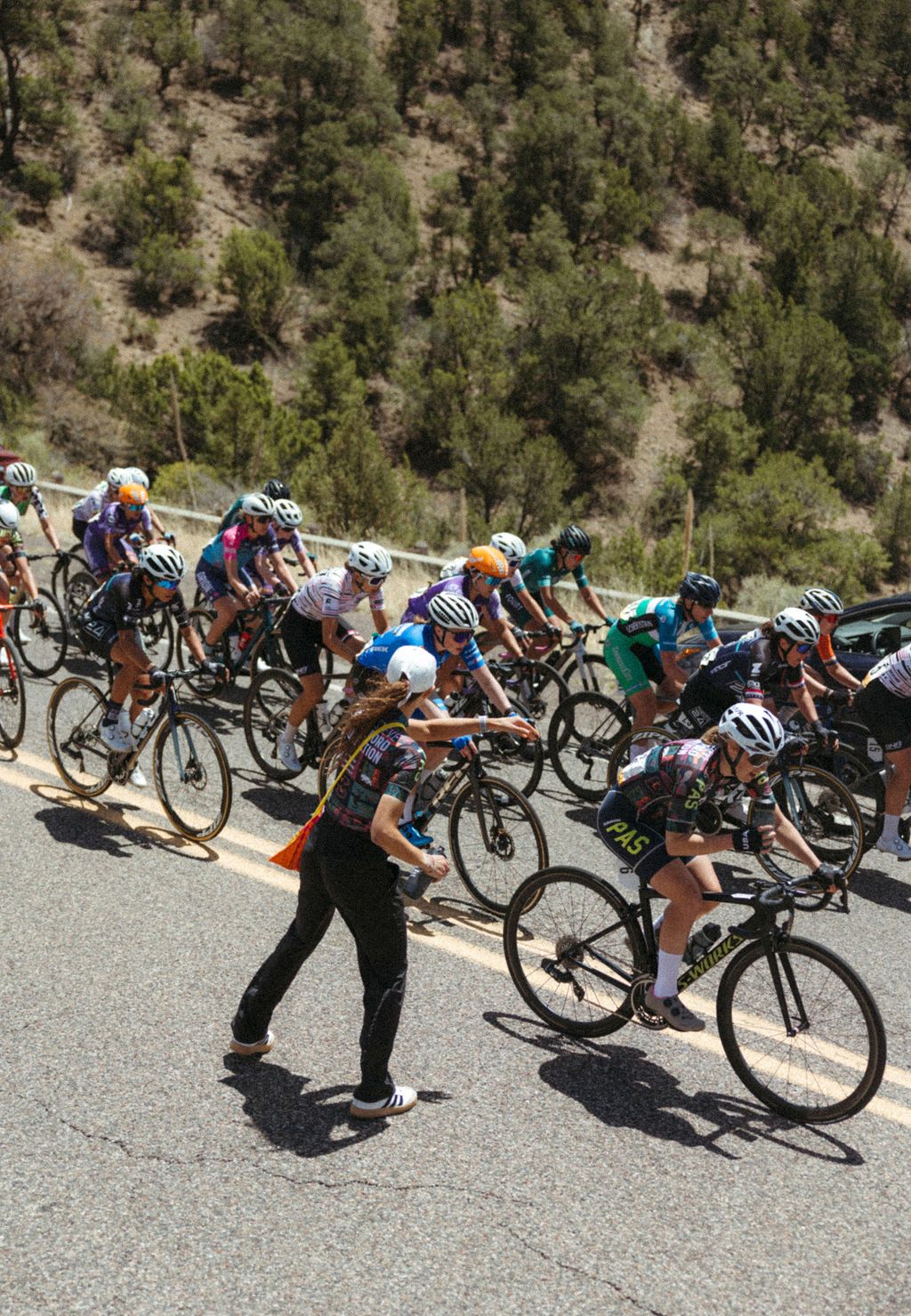 Professional cycling race peloton navigating mountain road turn with support staff
