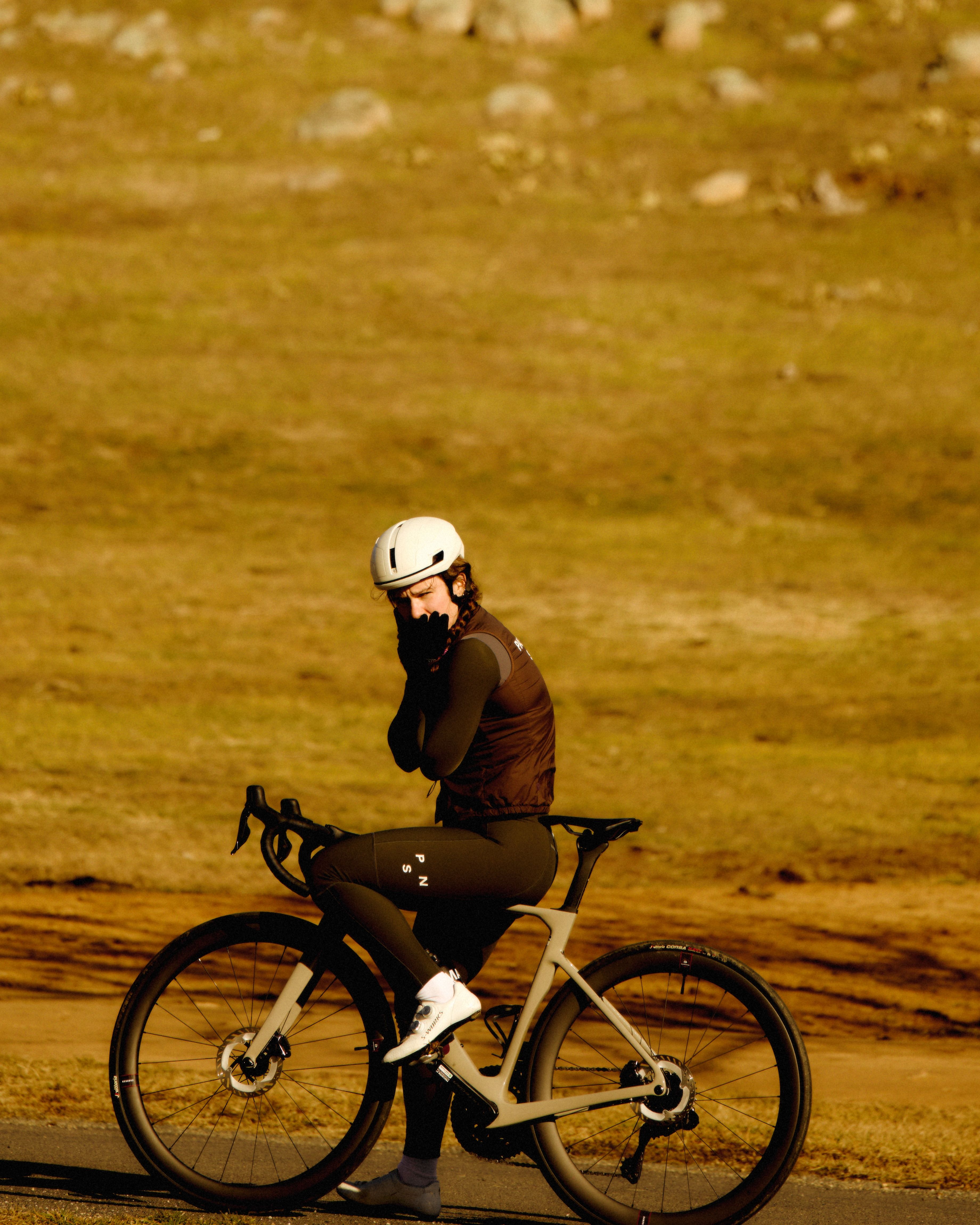 Model wearing brown cycling jacket with neck warmer on time trial bike in golden light