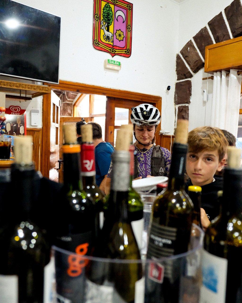 Cyclist wearing purple patterned jersey and helmet with child at Spanish tapas bar with wine bottles