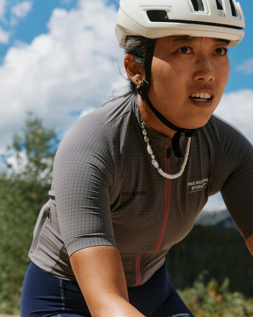 Model wearing grey grid-pattern cycling jersey with red zipper and white helmet outdoors