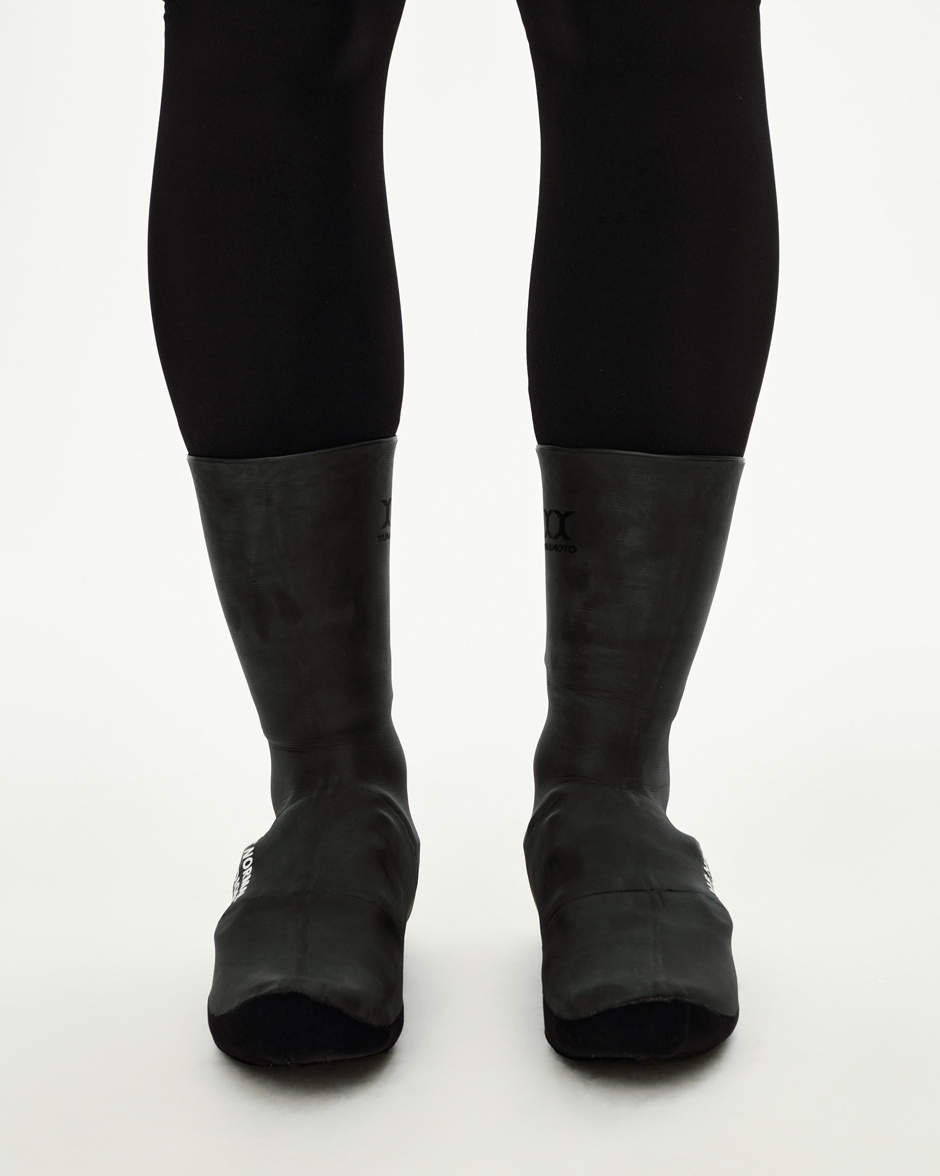 Black Logo Heavy cycling overshoes, front view on model as a pair with white logo print at toe