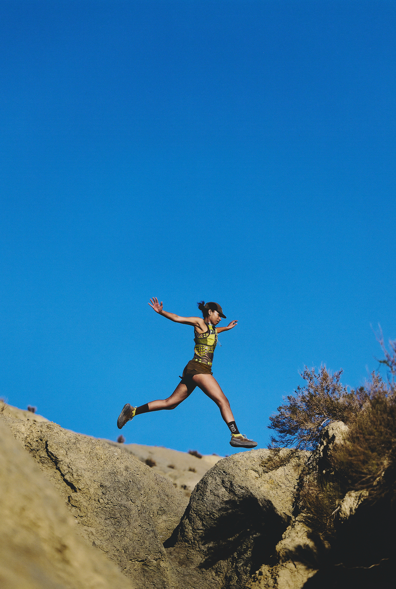 Model wearing yellow and black running apparel jumping between rocks against blue sky