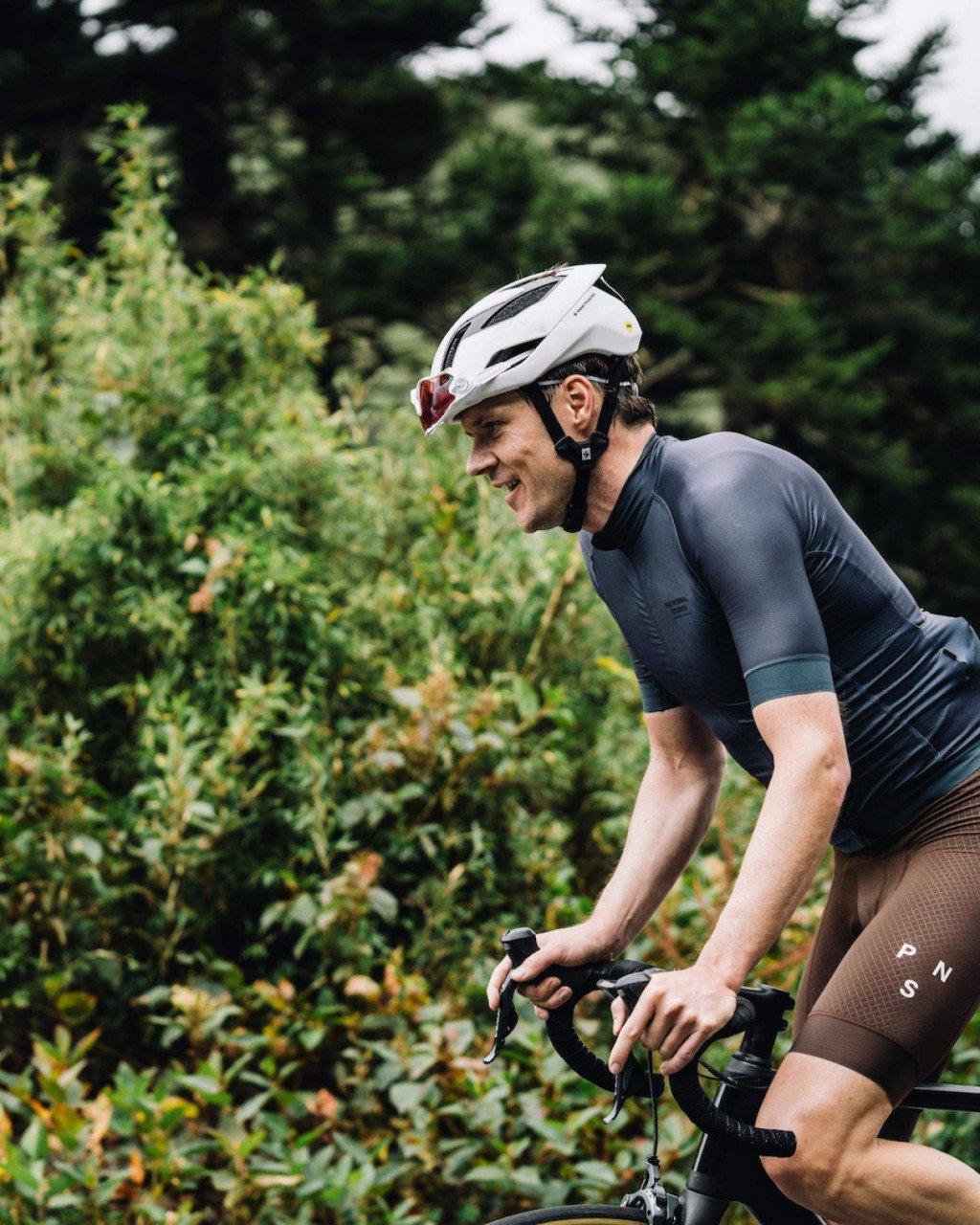 Model wearing black cycling skinsuit with aero helmet in cycling position outdoors