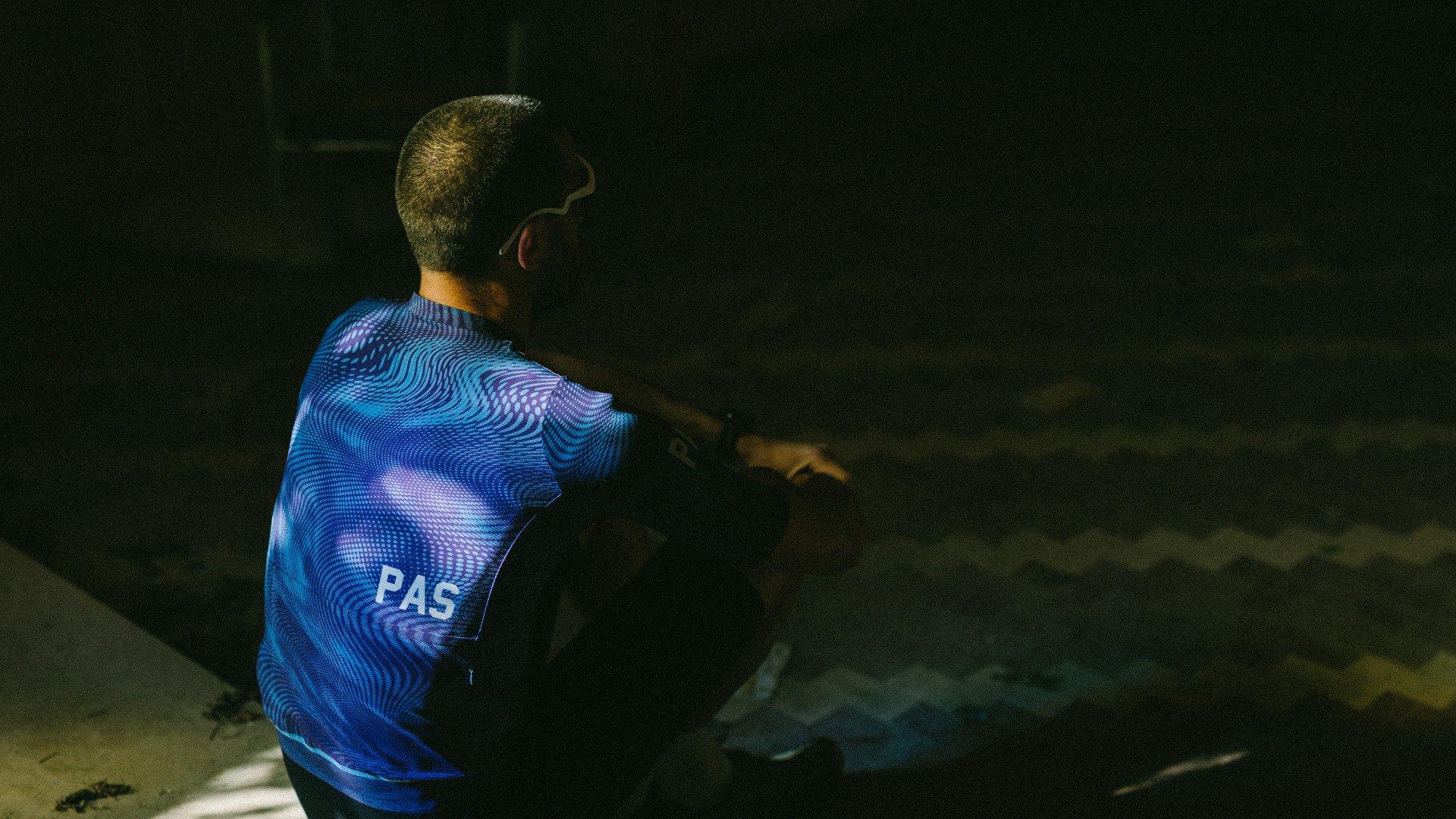 Model wearing blue PAS collection jersey with geometric wave pattern in dark tunnel setting