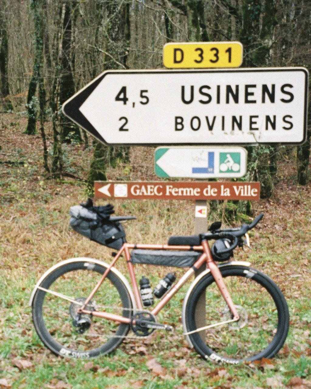 Pink gravel bike with bikepacking bags at French road signs in countryside