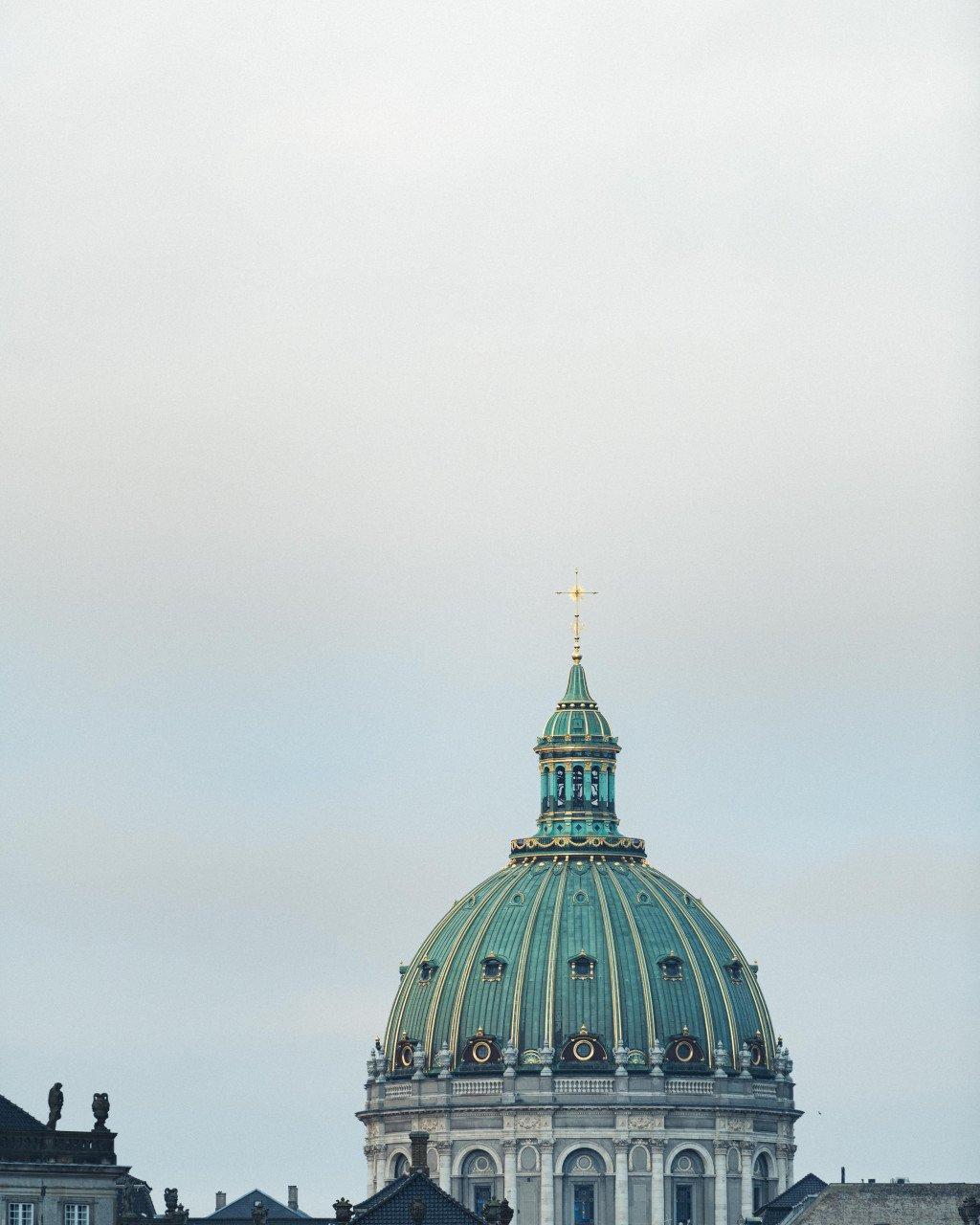 Green copper dome of historic church building with golden cross against overcast sky