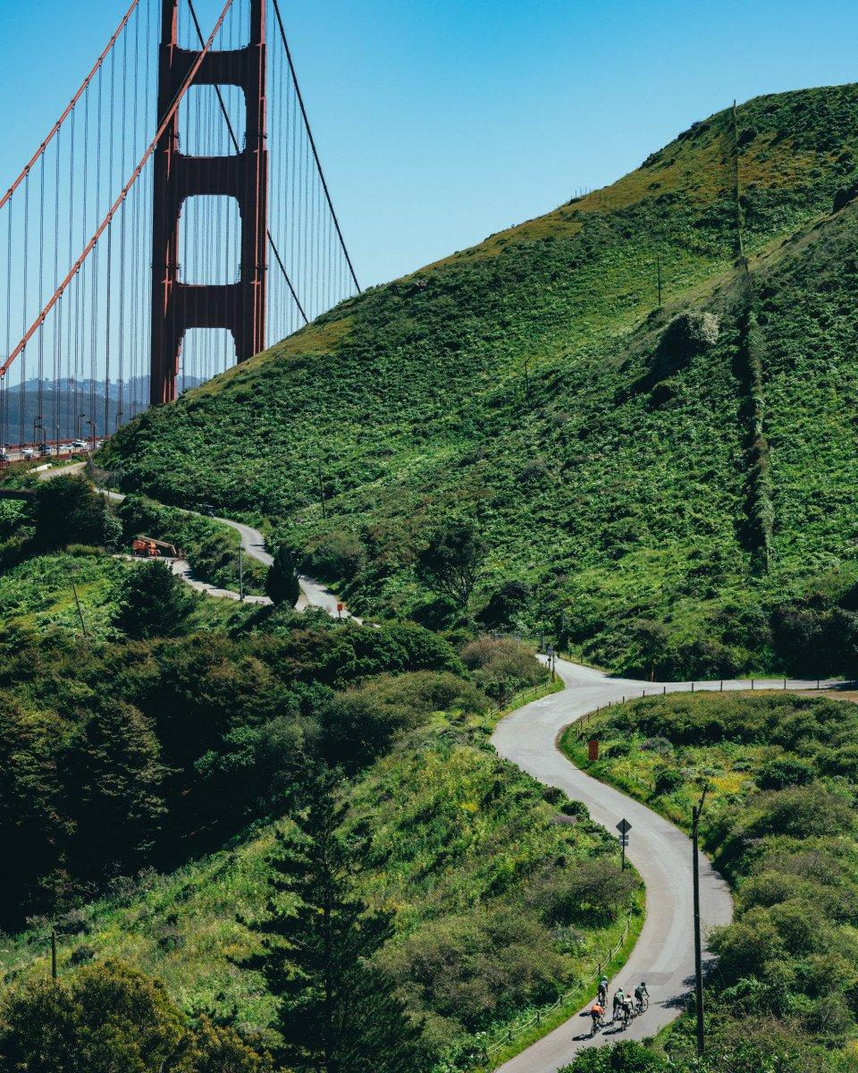 Cyclists on winding road through green hills with Golden Gate Bridge in background