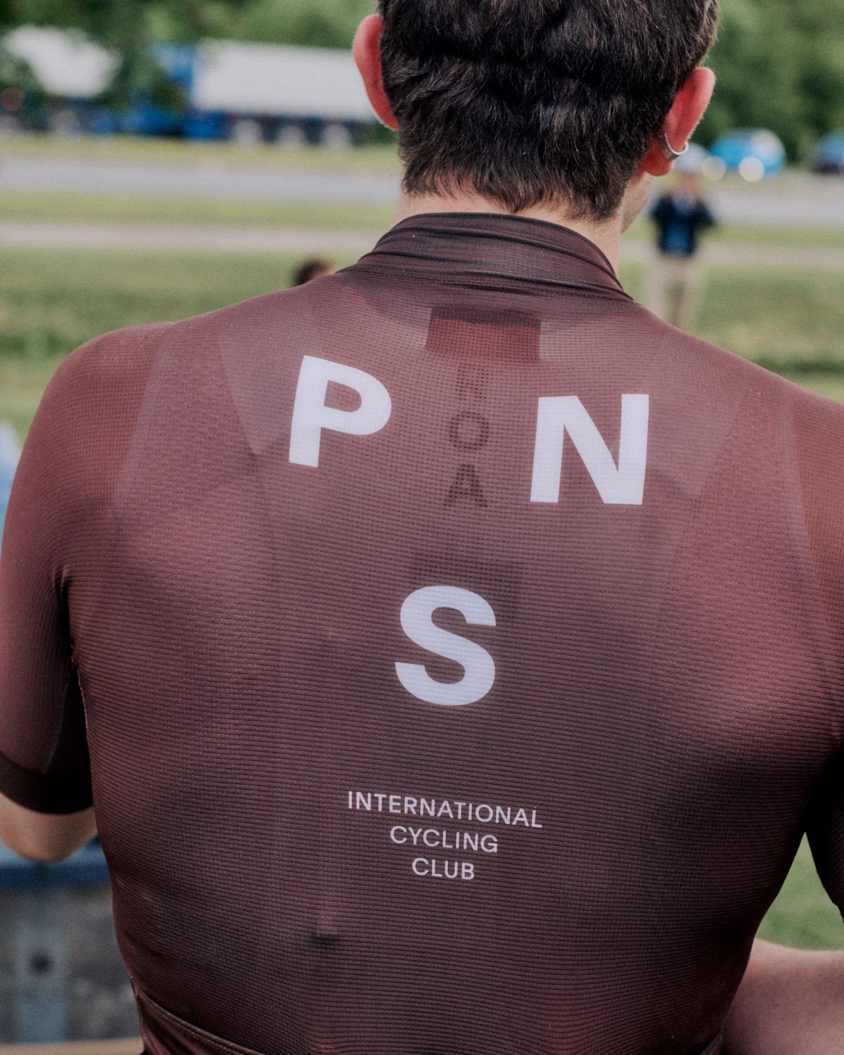 Model wearing burgundy cycling jersey with white lettering on back, viewed from behind outdoors