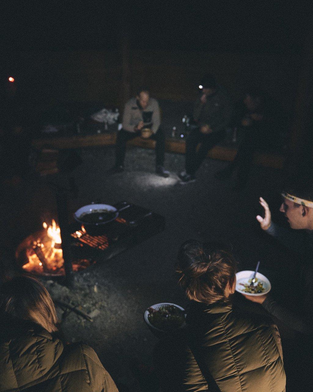 Cyclists gathered around campfire at night during bikepacking adventure
