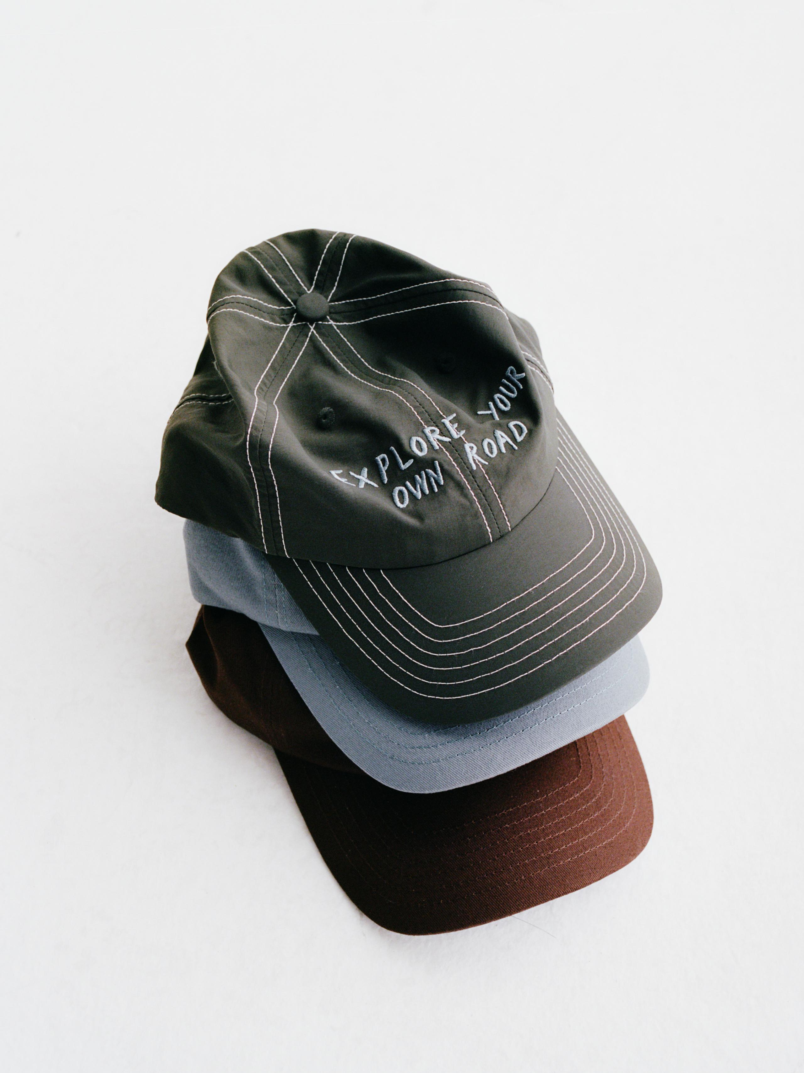 Dark Olive Off-Race cap, stacked with other caps showing white embroidered text